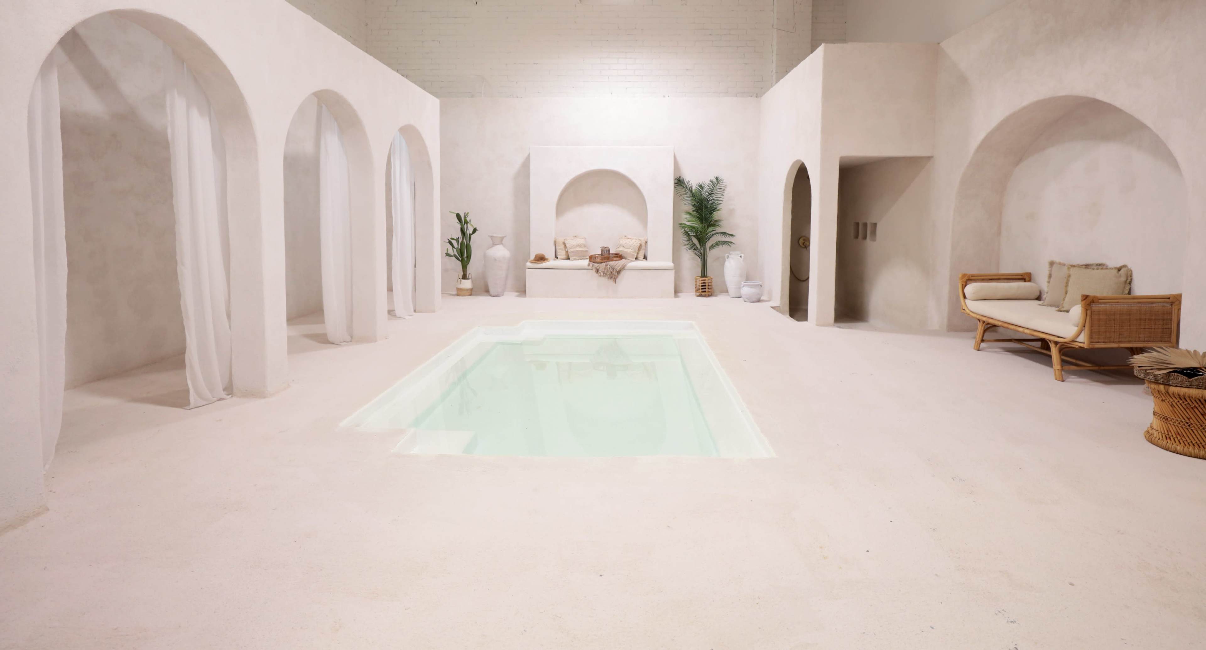 The scene features a minimalist interior with a shallow pool surrounded by white walls, arches, and neutral furnishings.