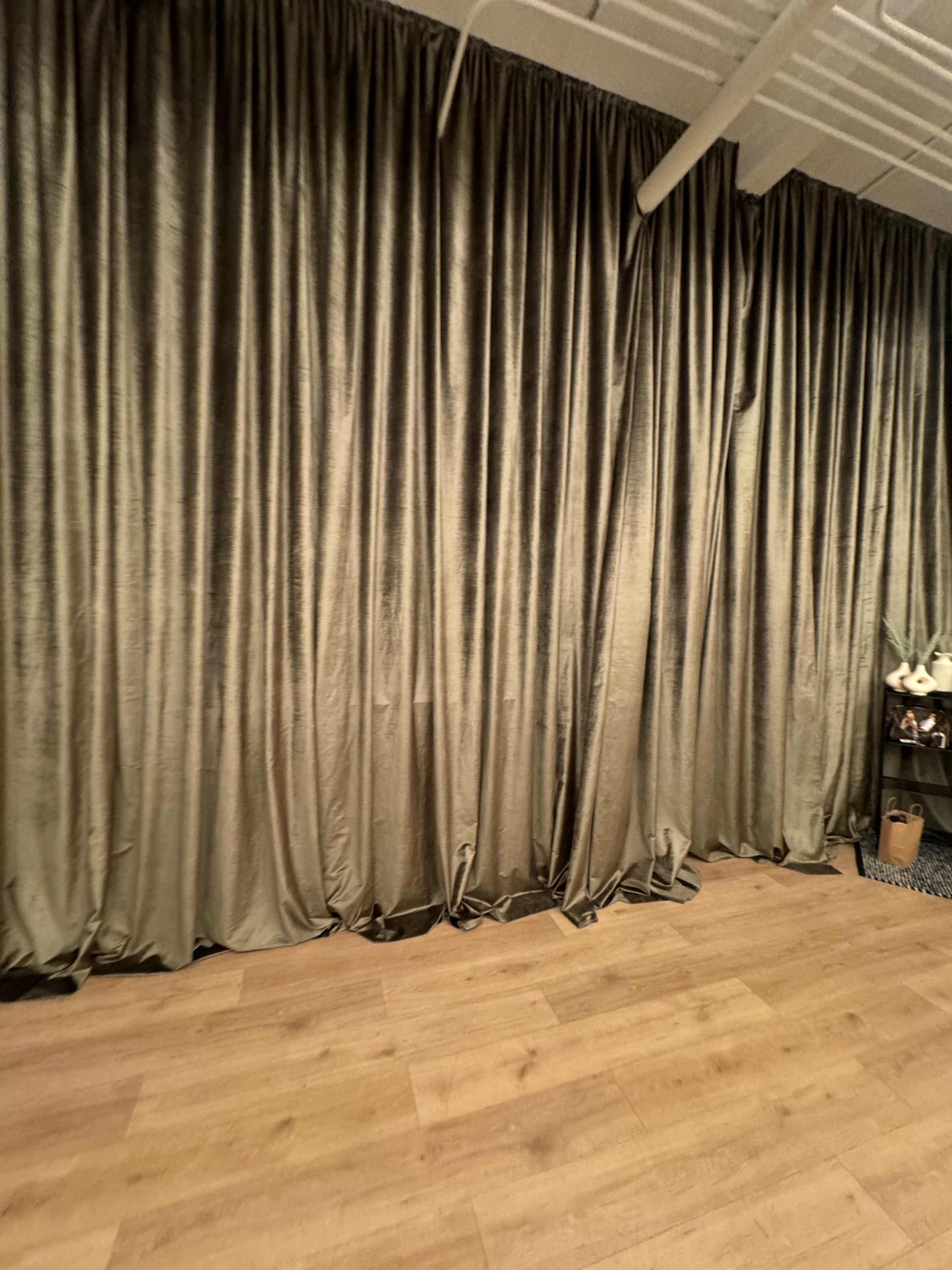 The image shows a spacious room with a floor covered in wood and a large, draped curtain in a muted tone along one wall.