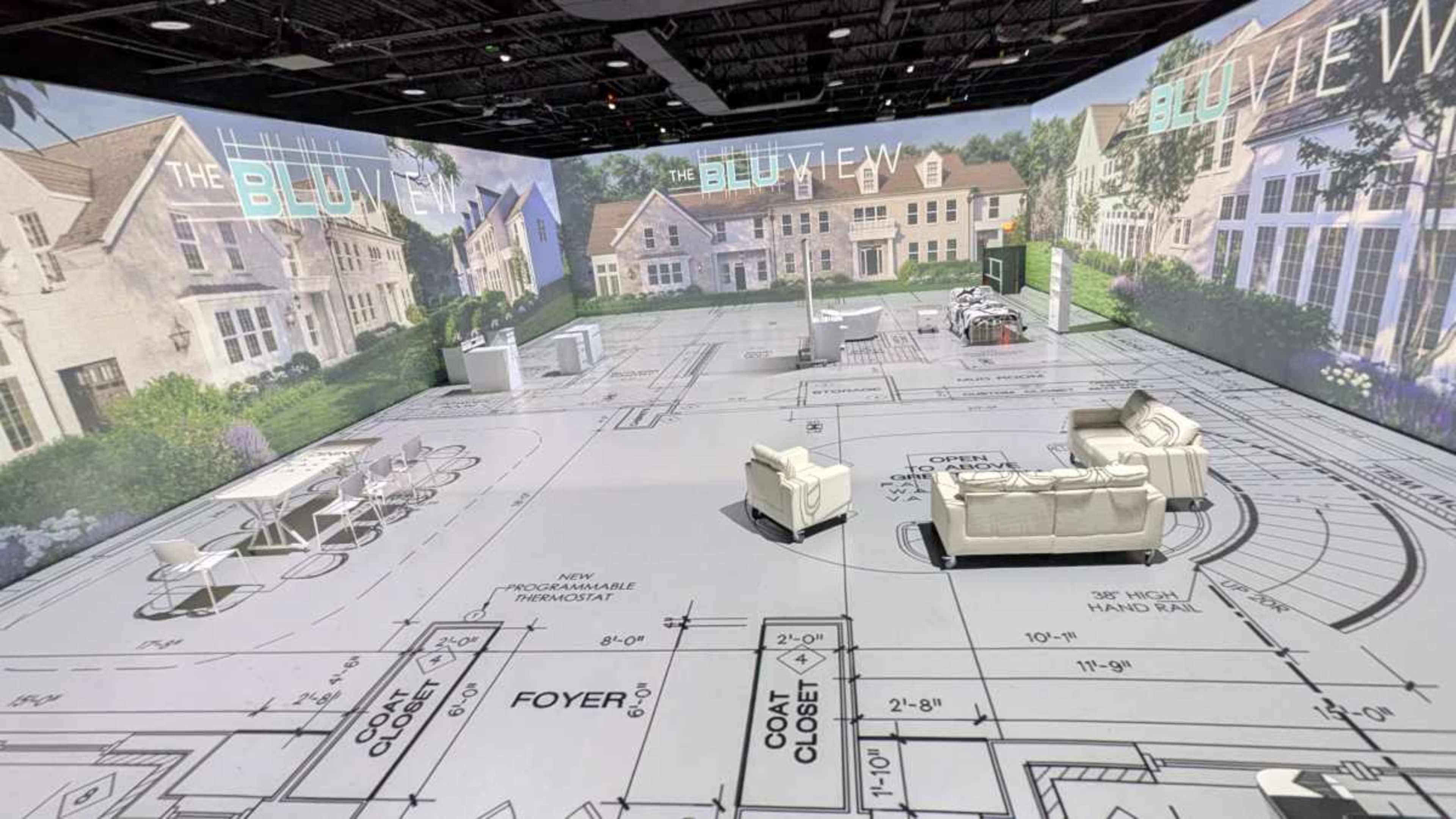 The image depicts a large, open space designed to resemble a blueprint of a house, featuring various rooms and furniture layouts projected onto the floor and walls.