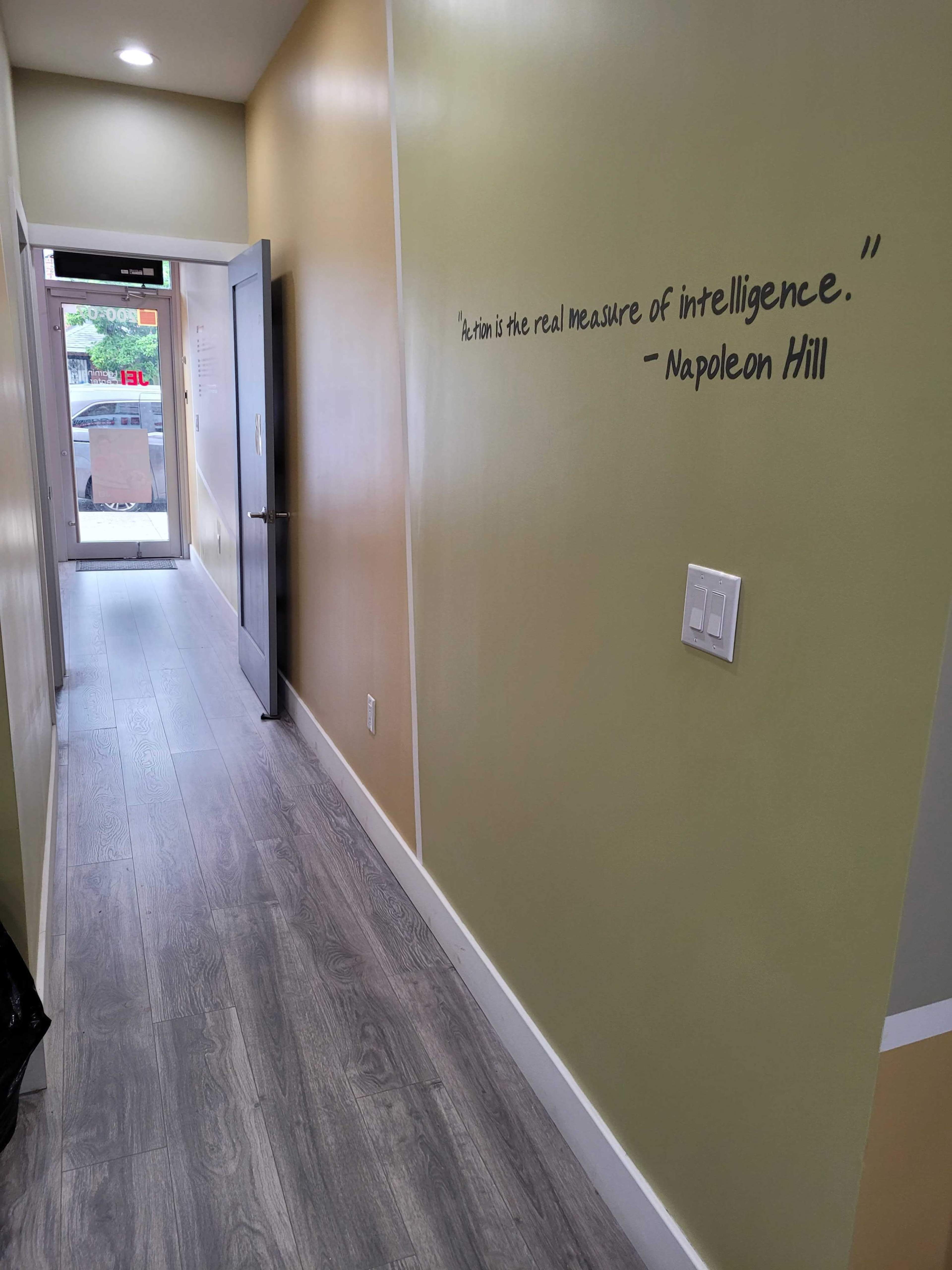 A narrow hallway with light green walls and a quote by Napoleon Hill painted on the wall, leading to a glass door at the far end.