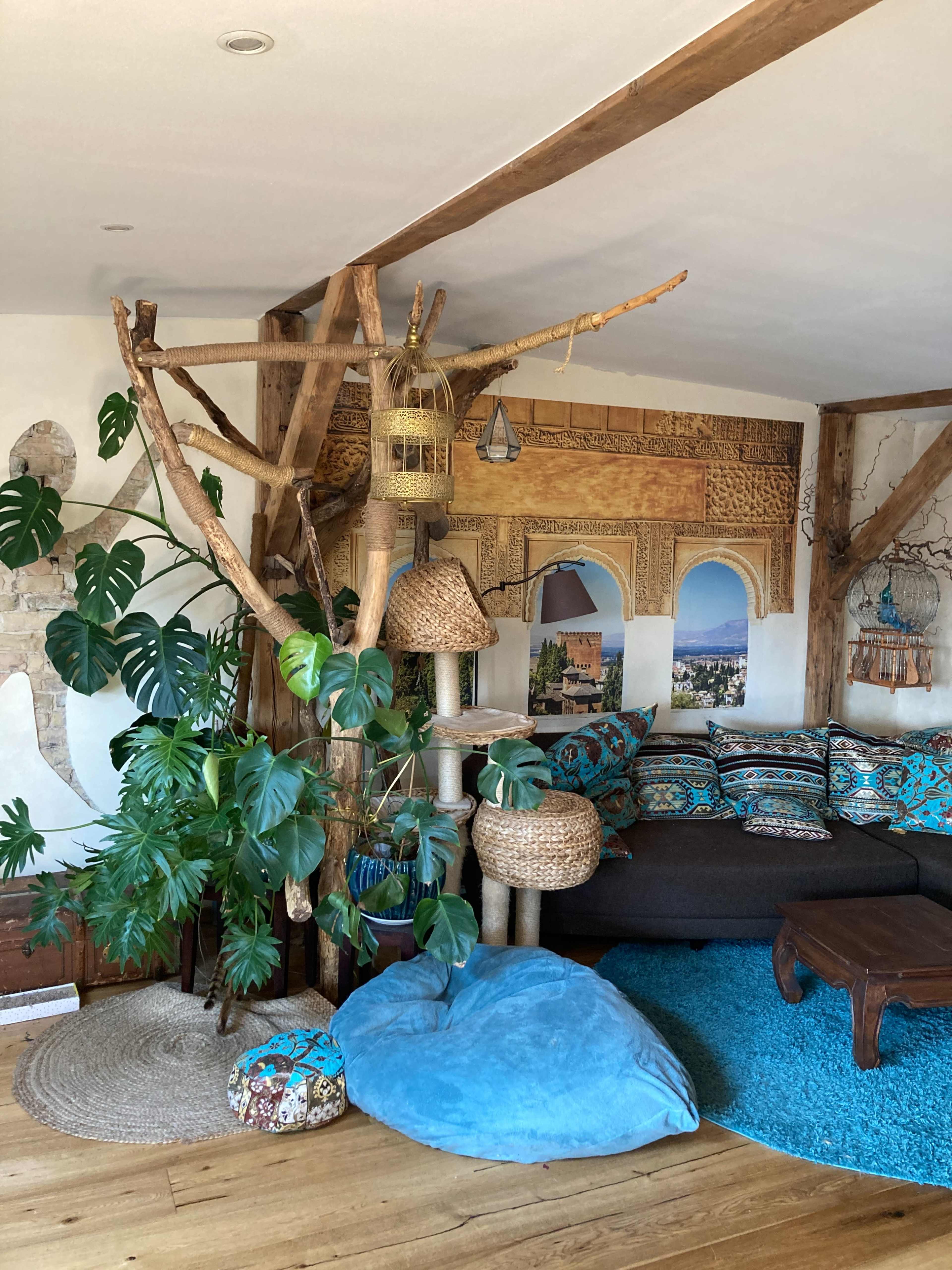 The scene shows a cozy living room featuring a large tree structure, a collection of woven baskets, a blue bean bag chair, and a sofa with colorful cushions.