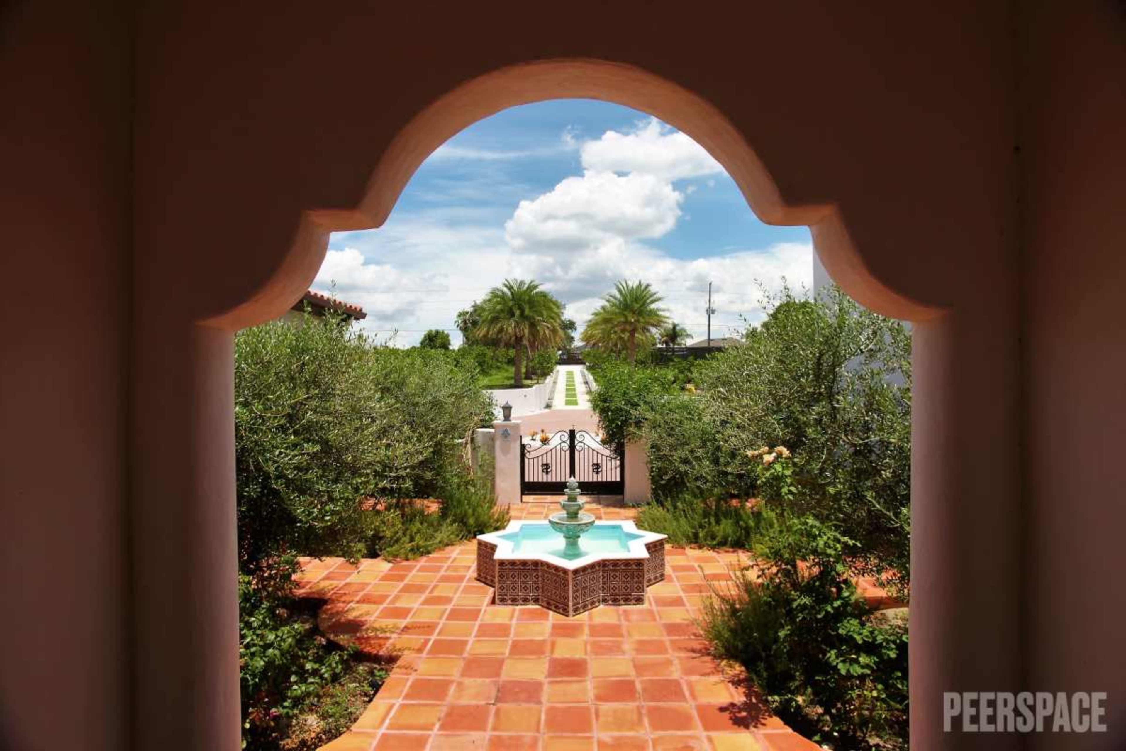 A view of a garden pathway leading to a fountain, framed by an archway.