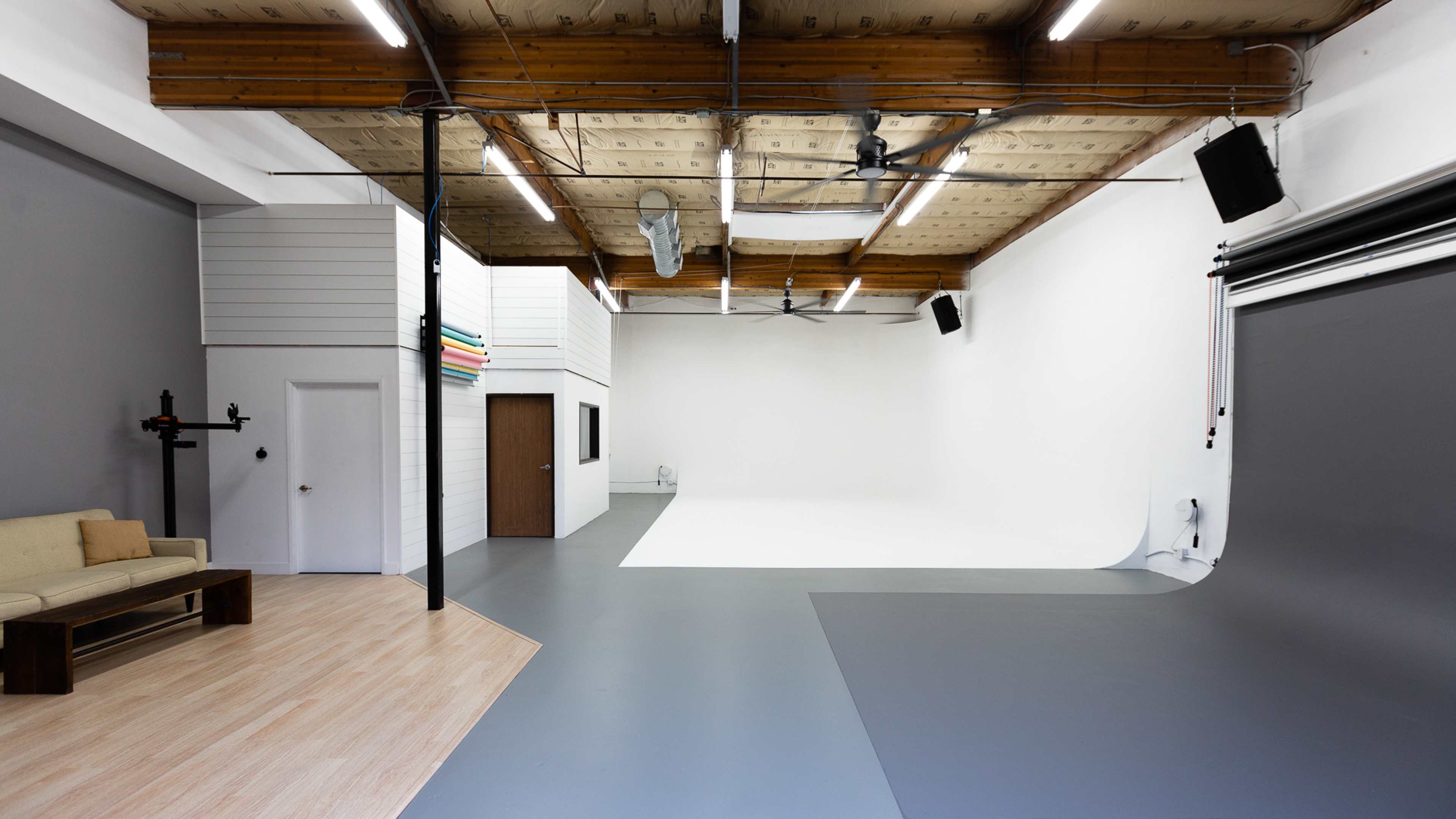 An empty photography studio featuring a gray floor, a seamless backdrop, and a seating area with a couch.