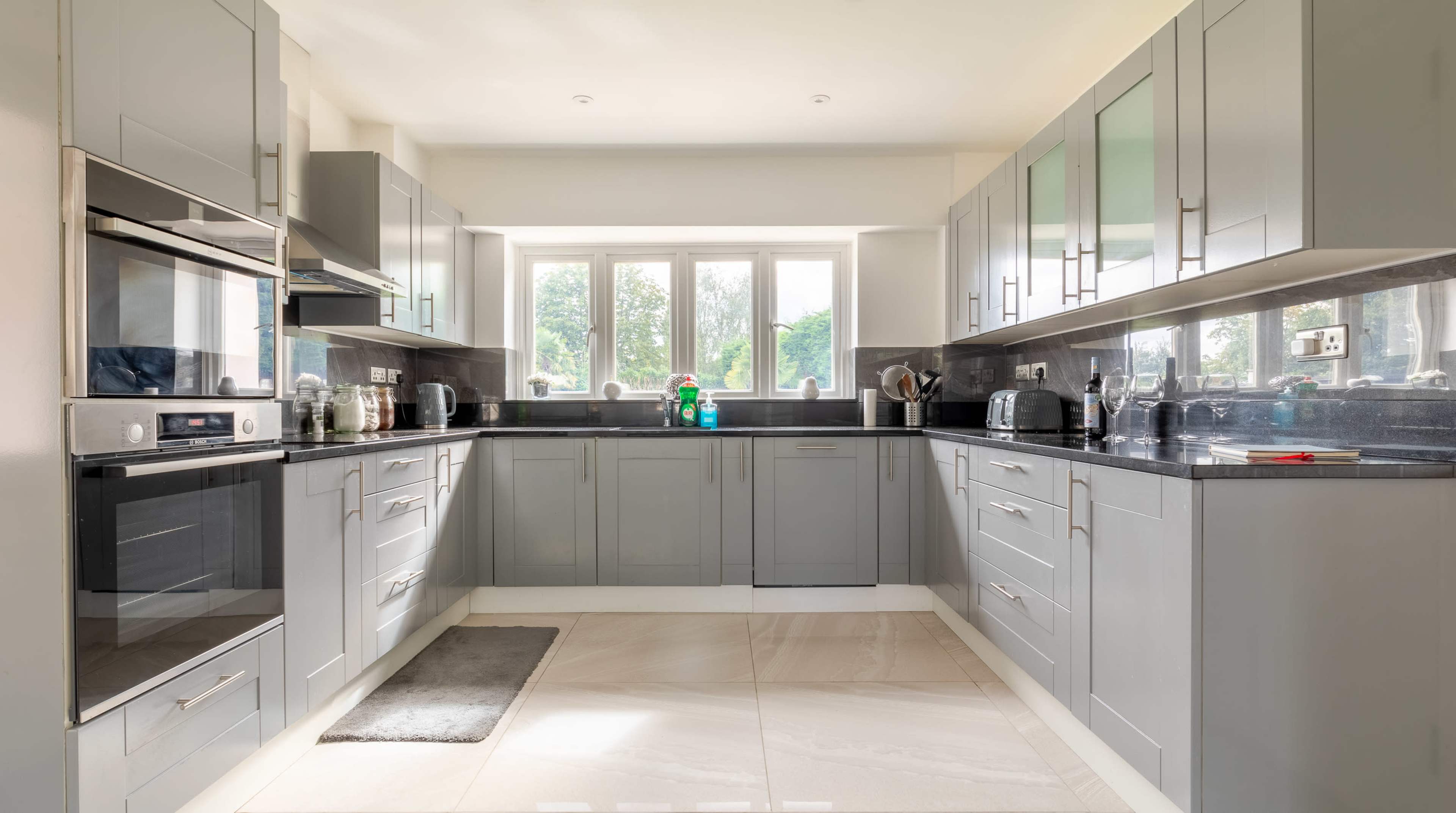 A modern kitchen features gray cabinetry, stainless steel appliances, and a spacious layout with a tiled floor.