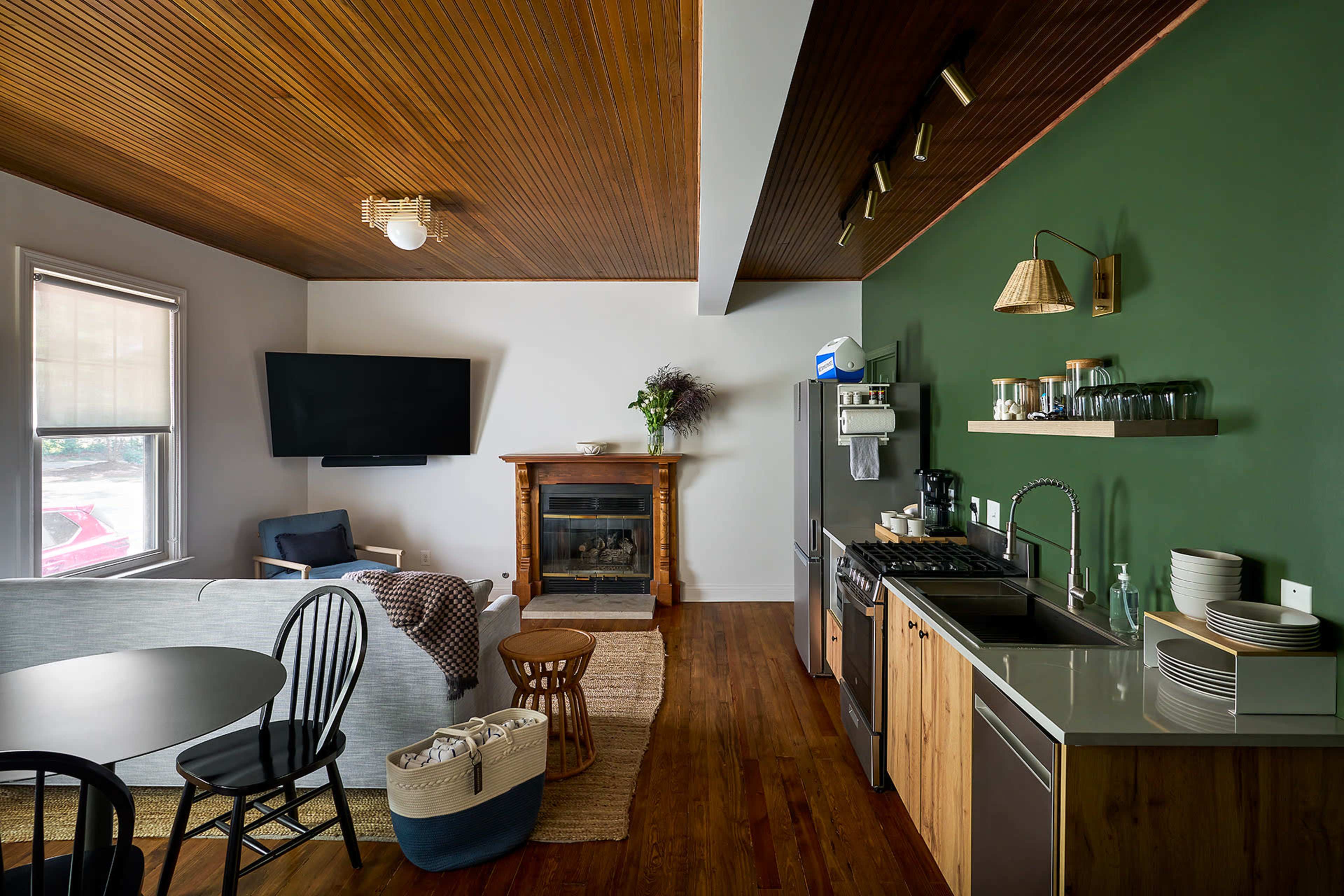 A modern kitchen and living area with a green accent wall, a dining table, and a fireplace.