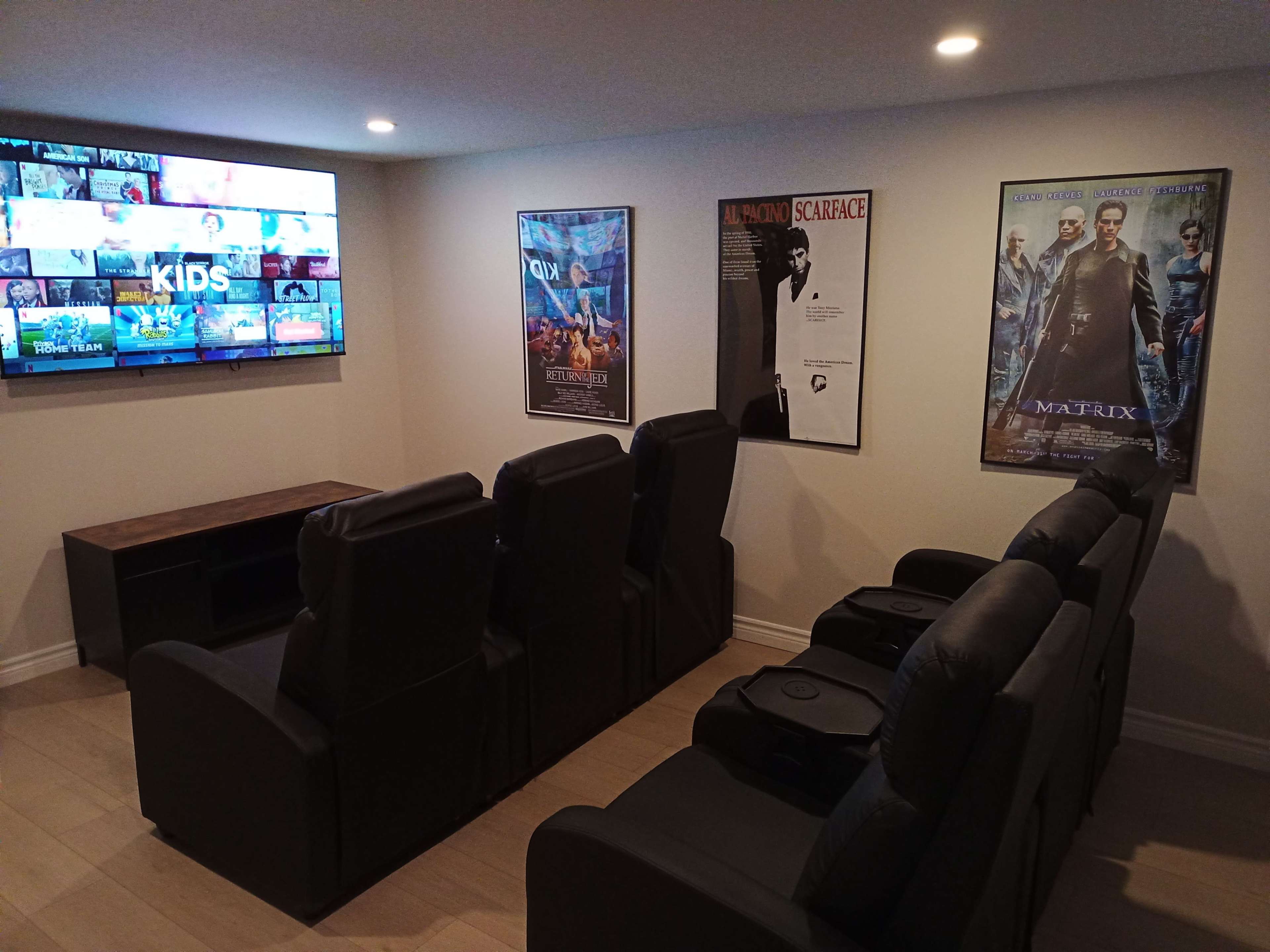 A home theater with black reclining chairs facing a large screen, flanked by movie posters on the walls.