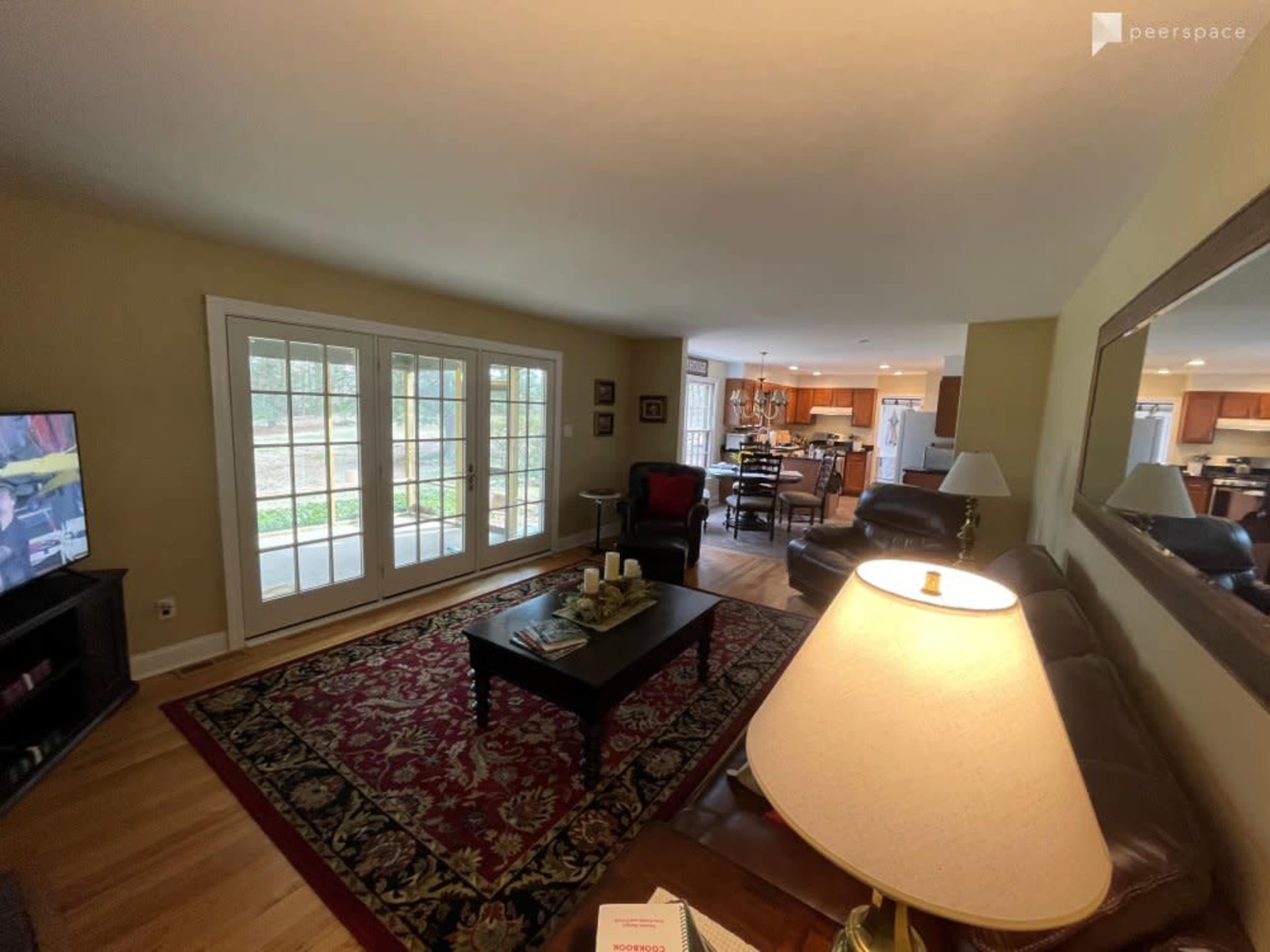 A well-lit living room features a coffee table on a patterned rug, two leather sofas, and large French doors opening to an outdoor area.