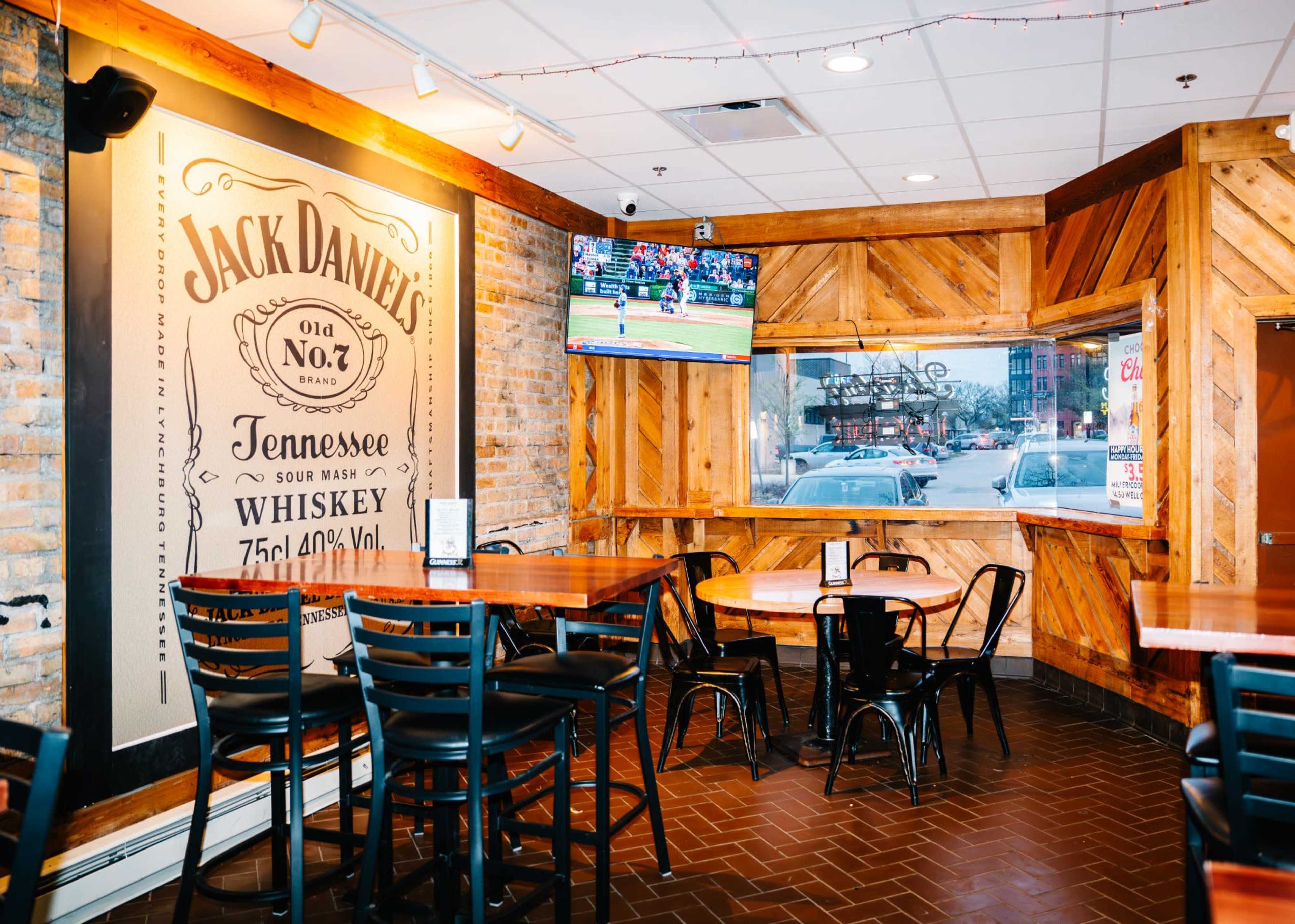 The image shows a bar interior with wooden paneling, tables and chairs, and a television displaying a sports game.