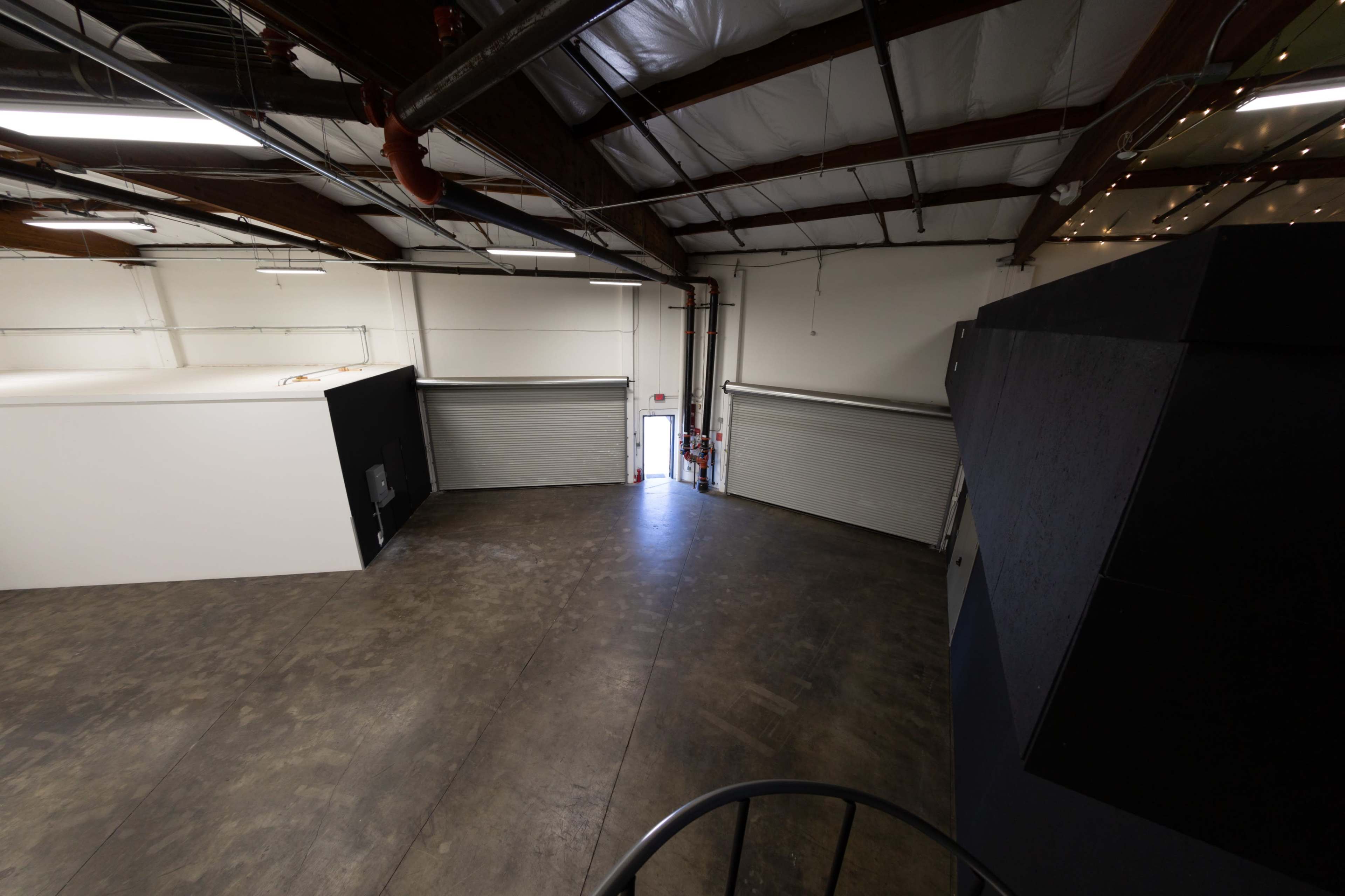 The image shows a spacious, industrial-style interior with high ceilings and large loading doors at one end.