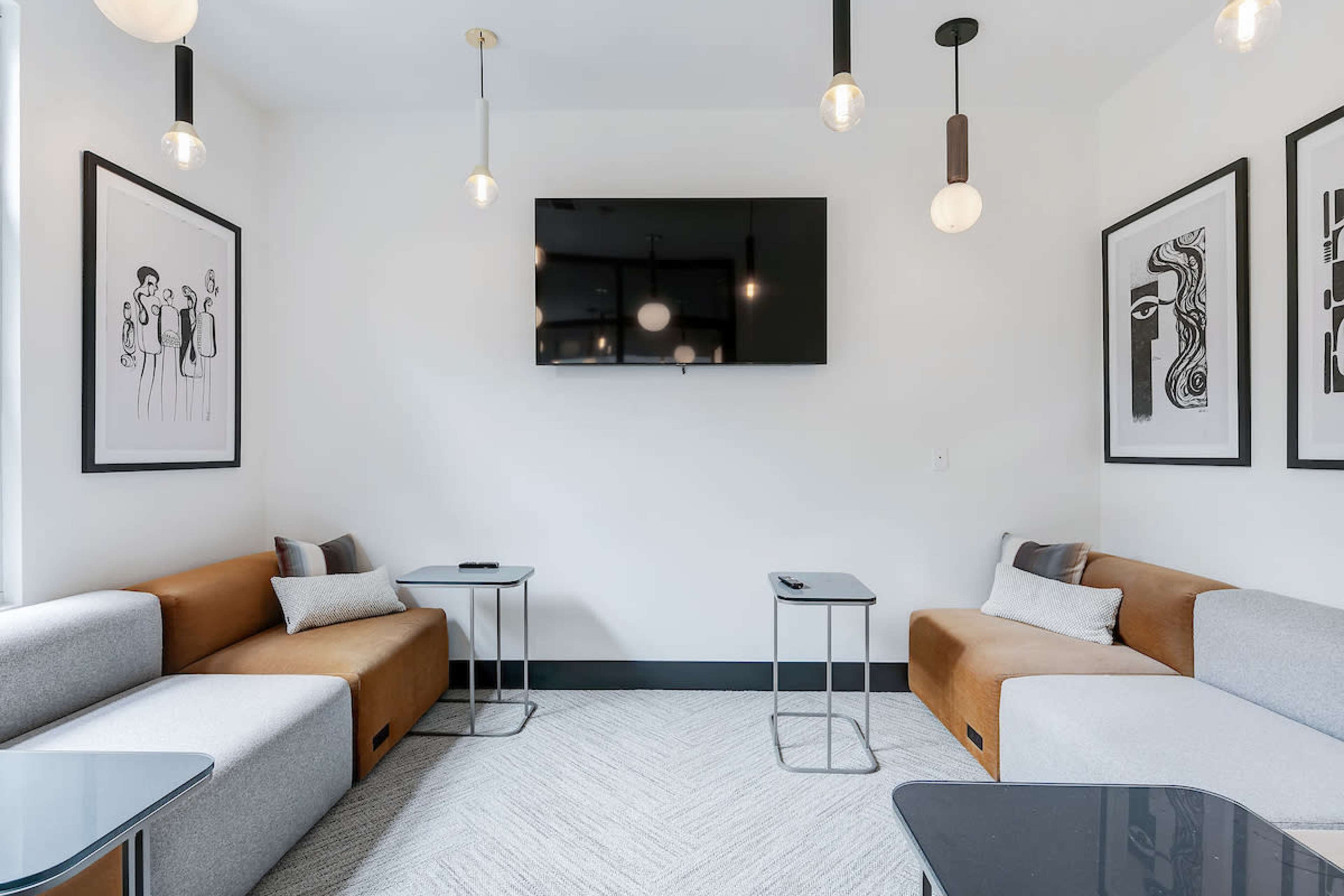 A lounge area features two modular sofas, small side tables, and a wall-mounted television, complemented by framed artwork.