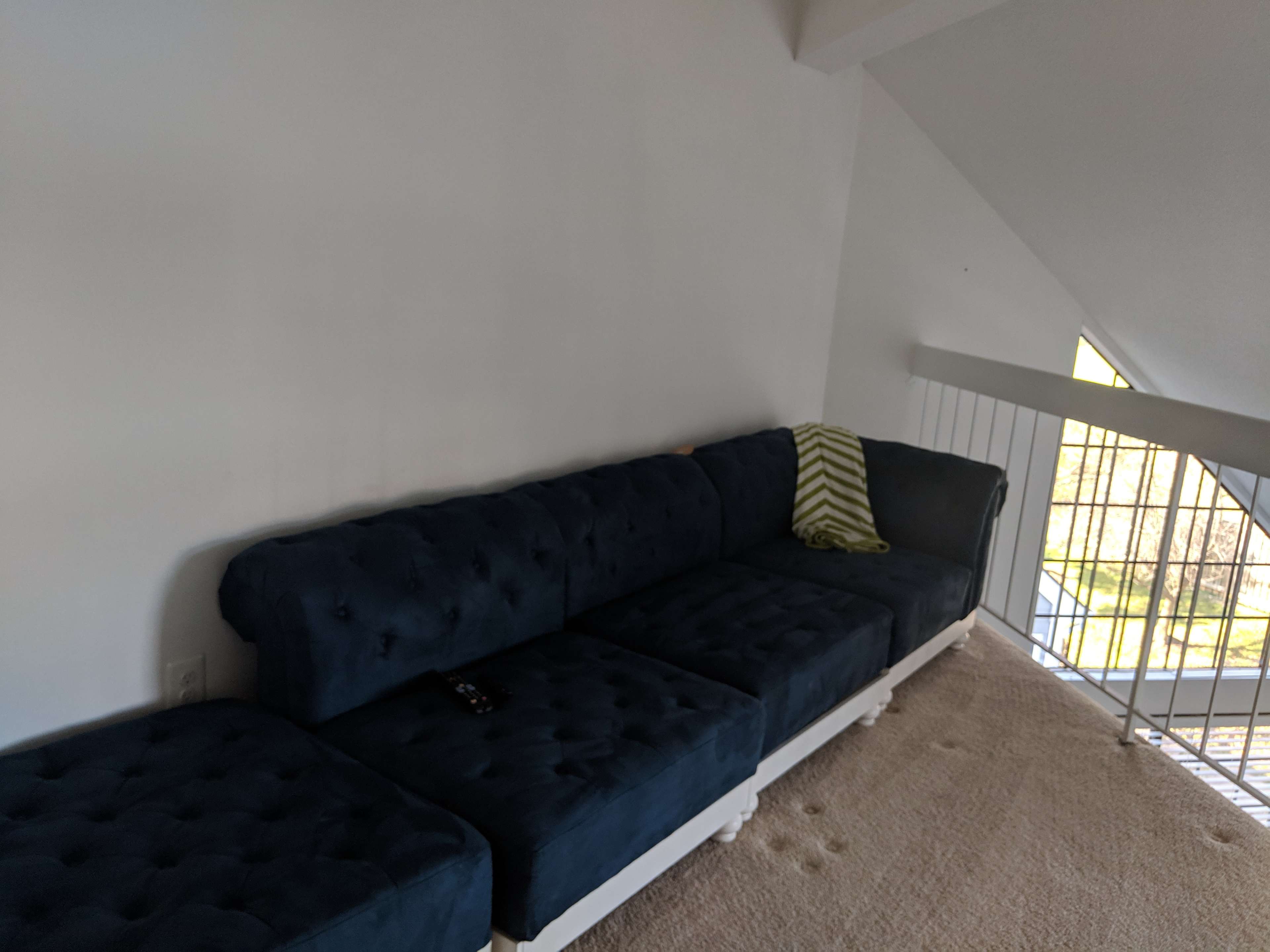 A dark blue tufted sectional sofa is placed against a white wall in a brightly lit room.