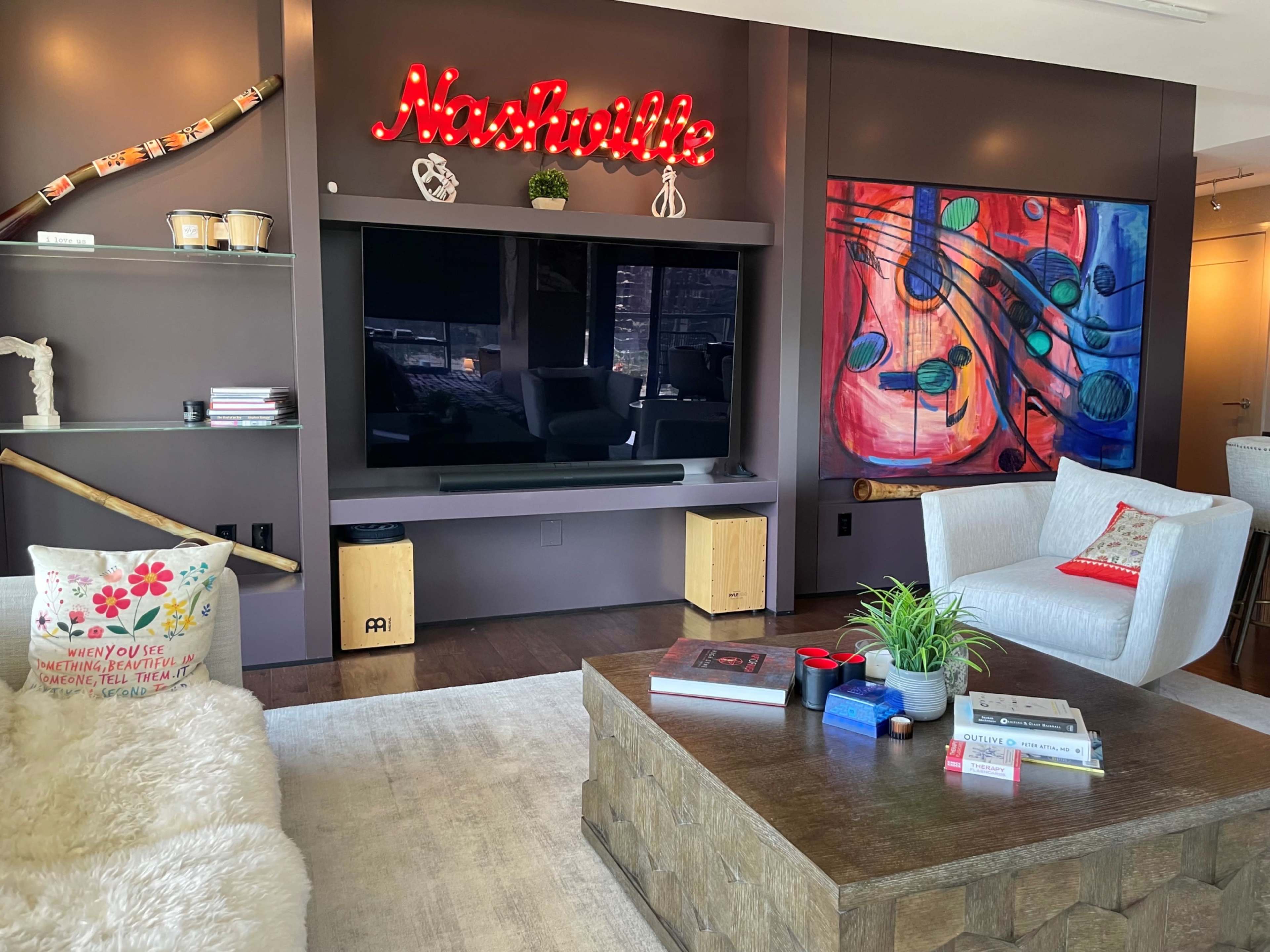 The living room features a television against a dark wall, accented with a neon "Nashville" sign, modern furniture, and decorative art.