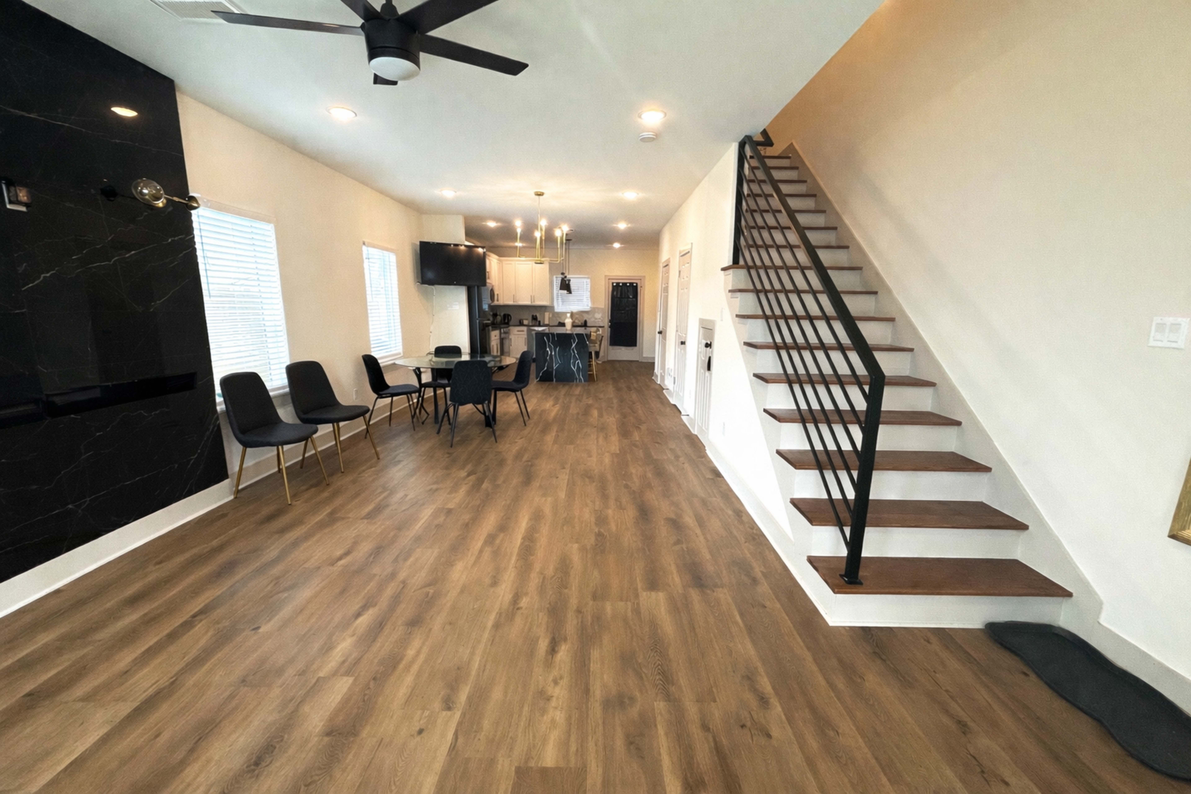 The image shows a modern interior with a staircase, dining area, and open kitchen, featuring wood laminate flooring and a black accent wall.