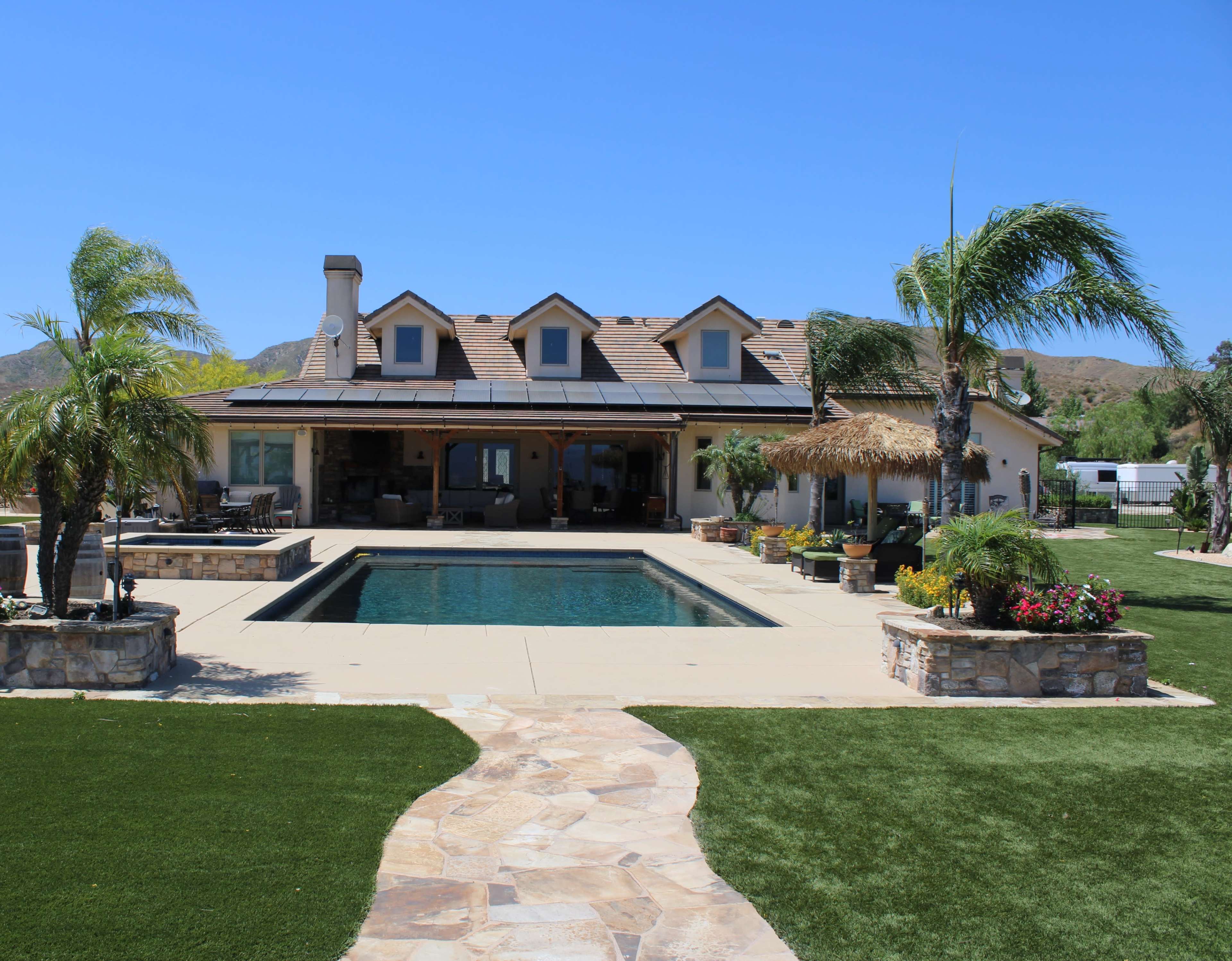 A single-story house with a pool and landscaped garden features a stone pathway leading to the entrance.