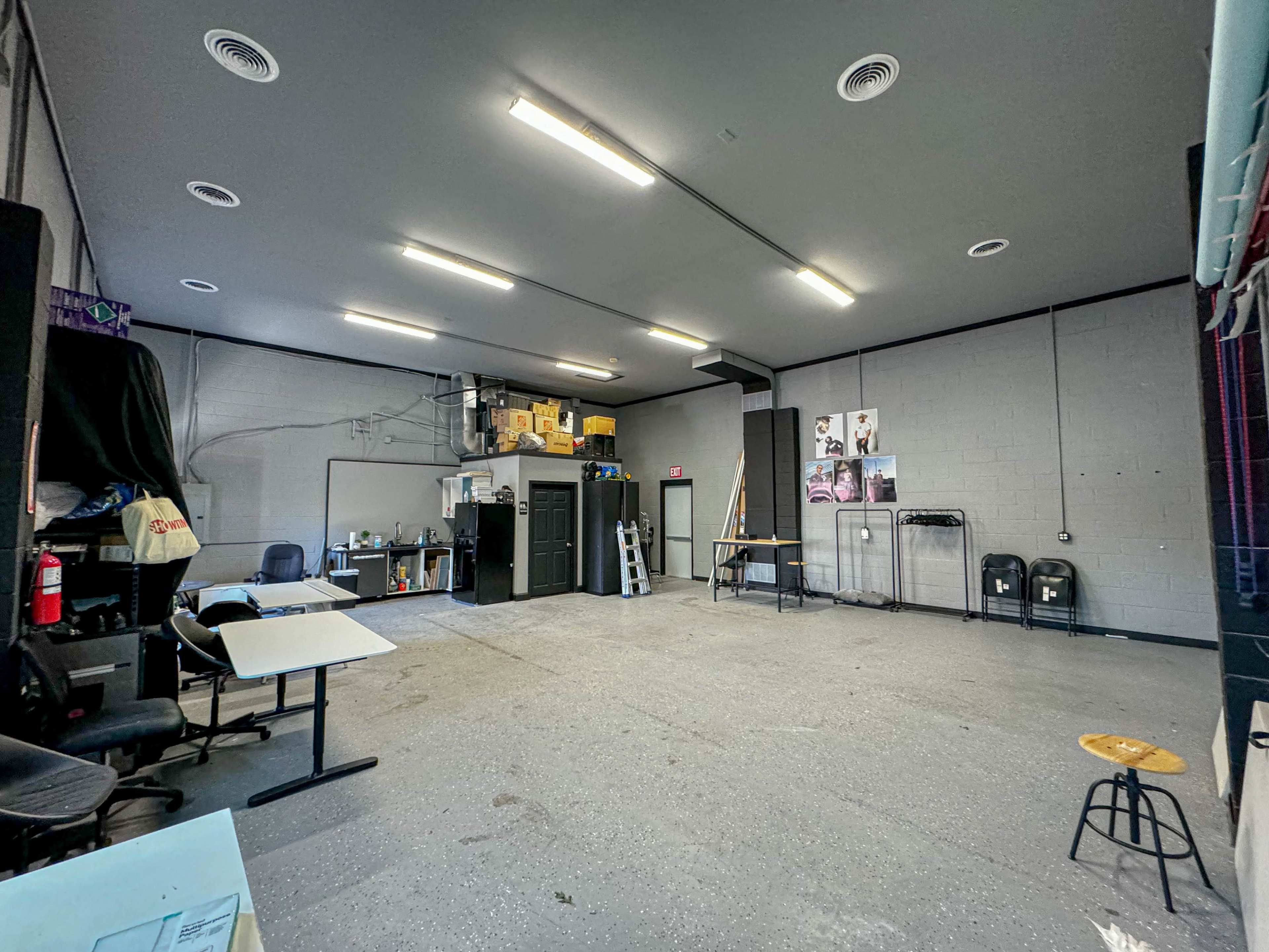 A sparsely furnished industrial space with gray walls, overhead lights, and some storage units and furniture scattered throughout.