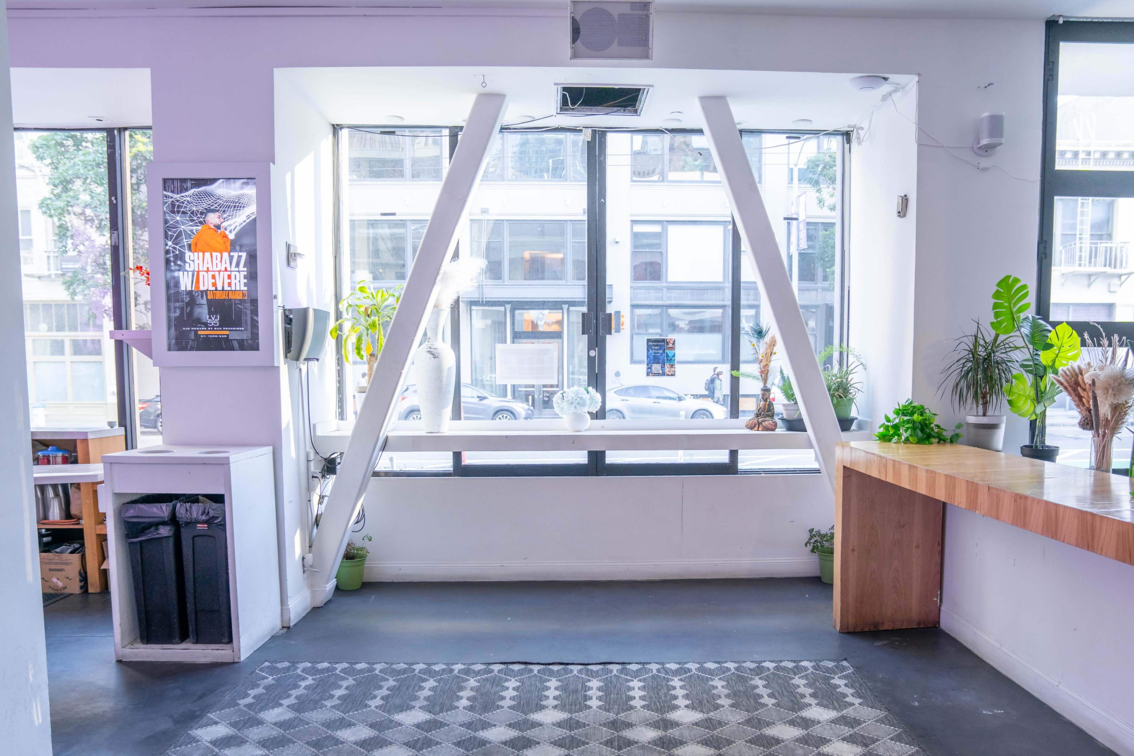 A bright, minimalistic interior space with large windows, wooden countertops, and decorative plants.