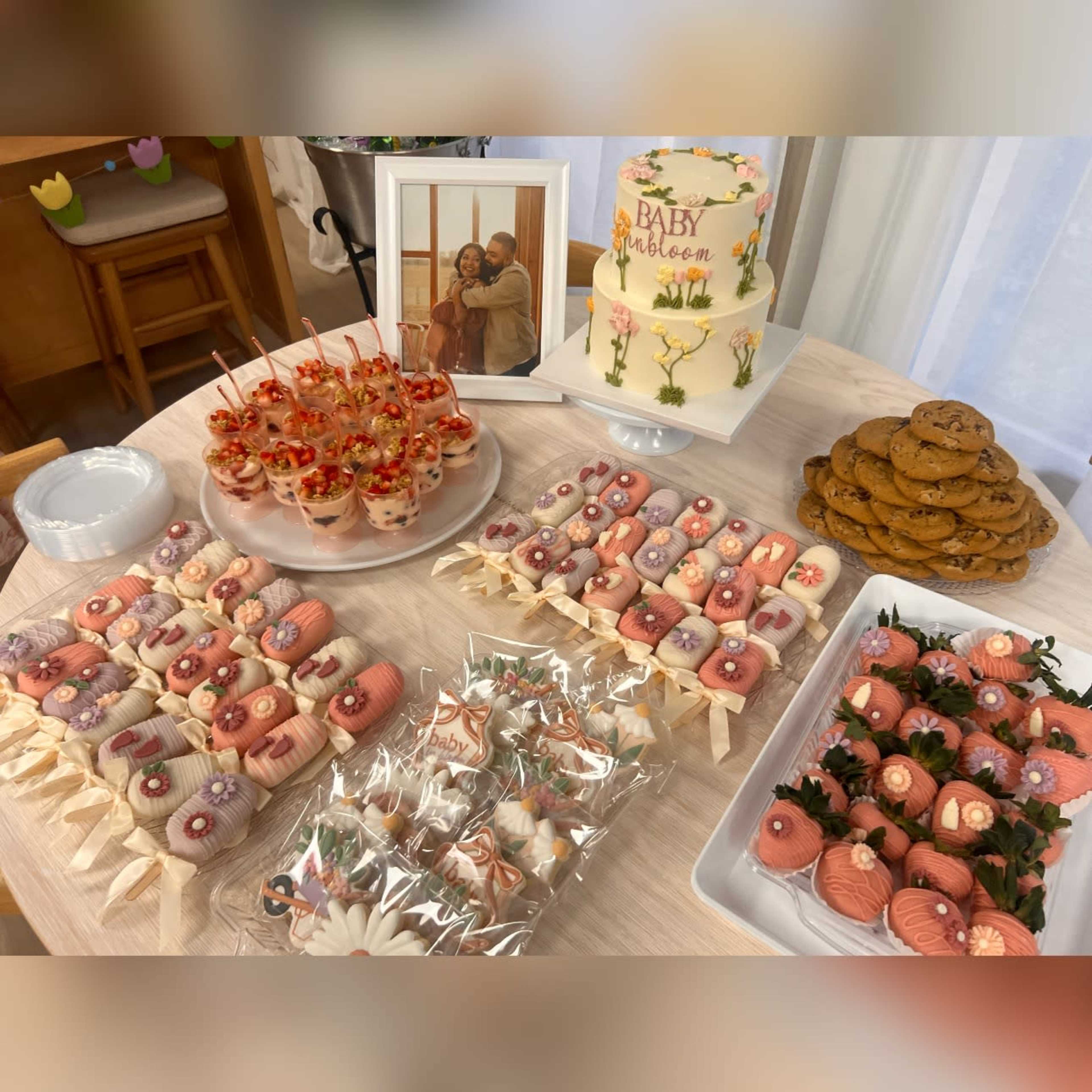 The image displays a dessert table featuring a variety of decorated treats, including cake pops, cupcakes, a cake labeled "BABY," and cookies, arranged on different platters.