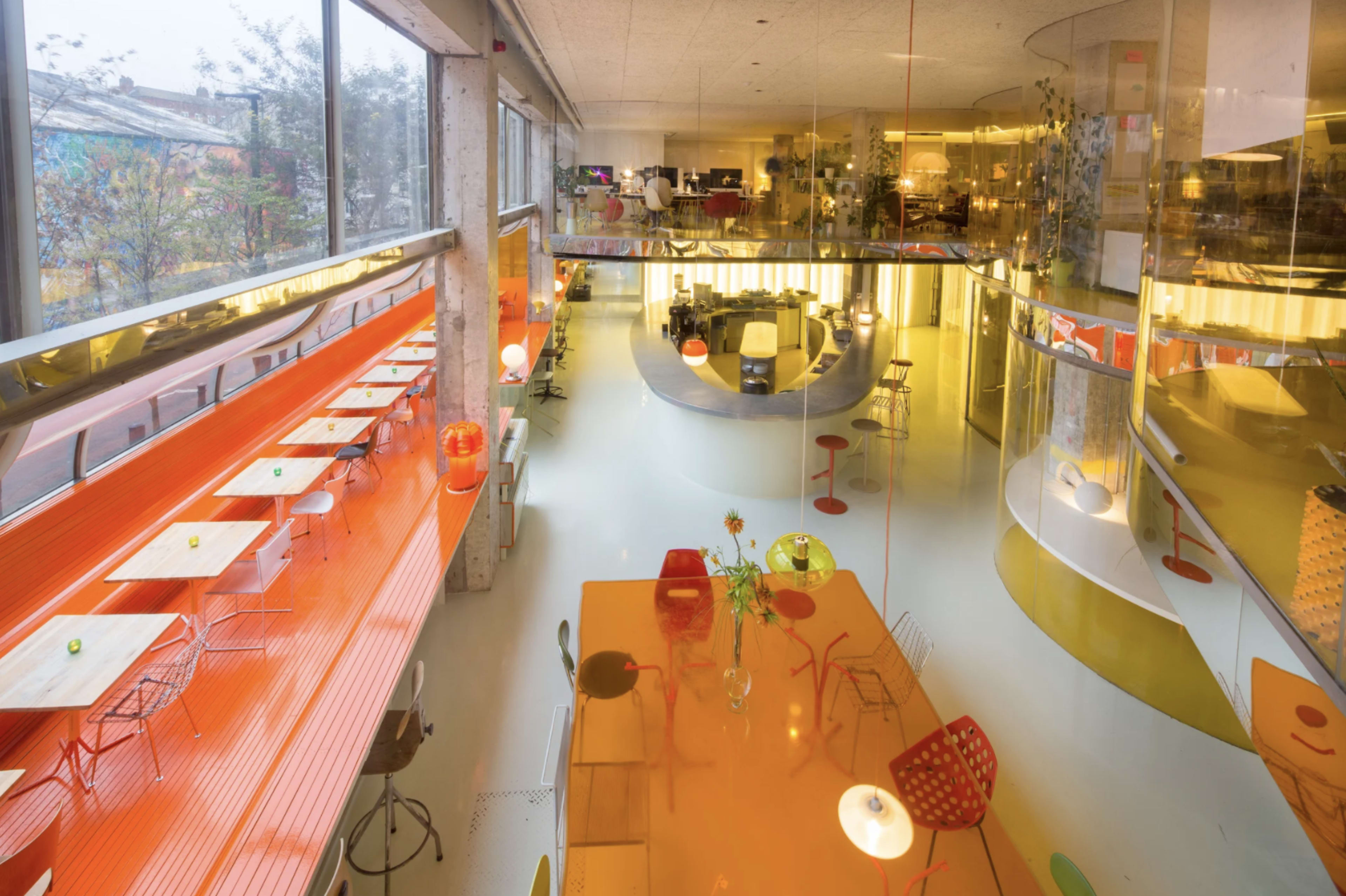 A modern, open-plan interior with colorful furniture and decorative elements, featuring a large communal table and seating areas.