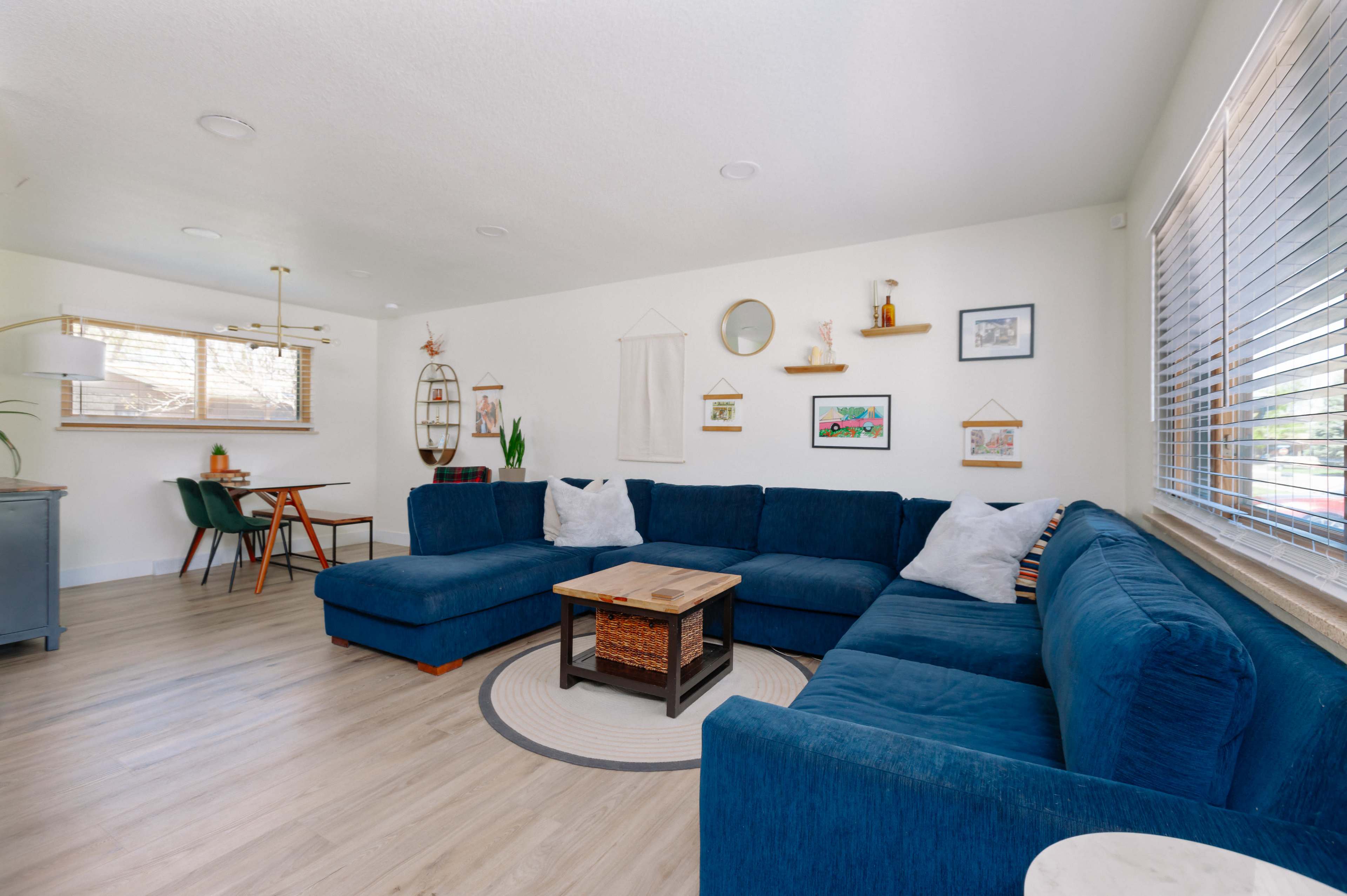 A spacious living room features a large blue sectional sofa, a wooden coffee table, and a dining area with green chairs.
