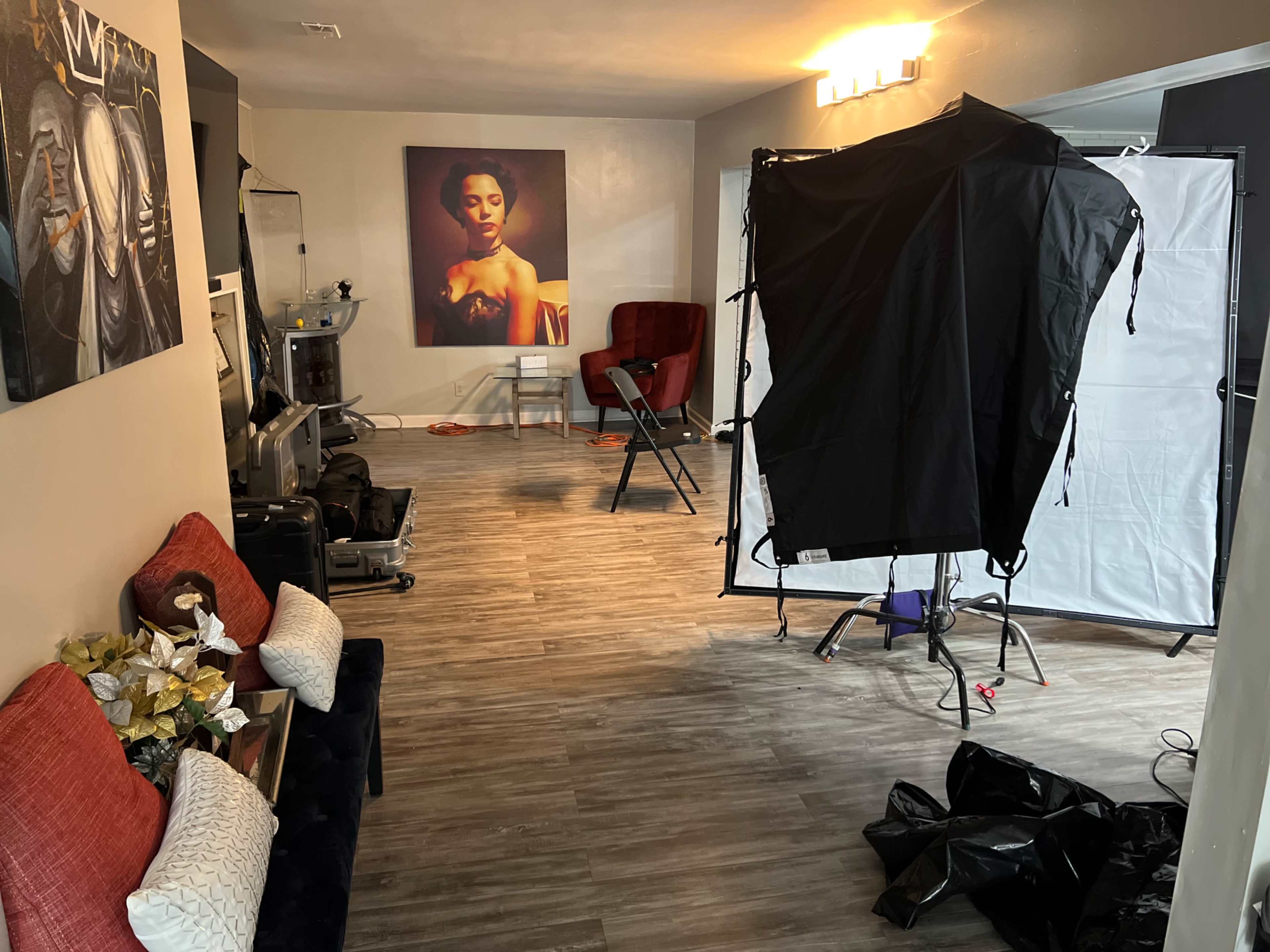 The image shows a photography studio with a chair, lighting equipment, and a large portrait on the wall.
