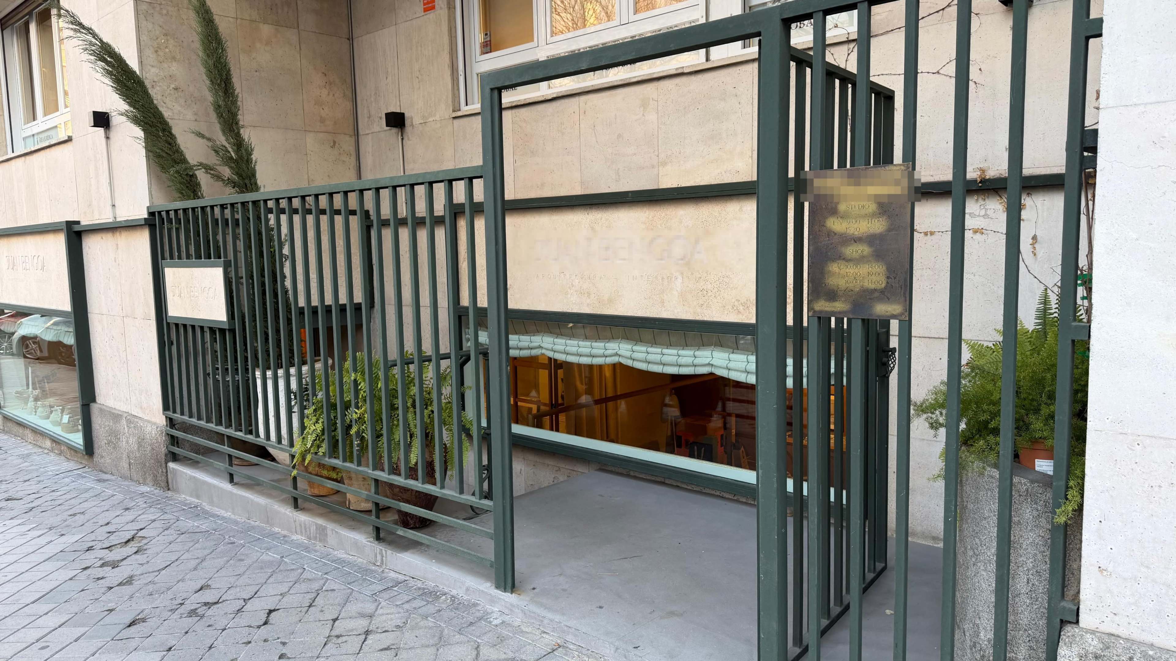 The image shows an entrance to a building with a gated structure and plants visible inside.