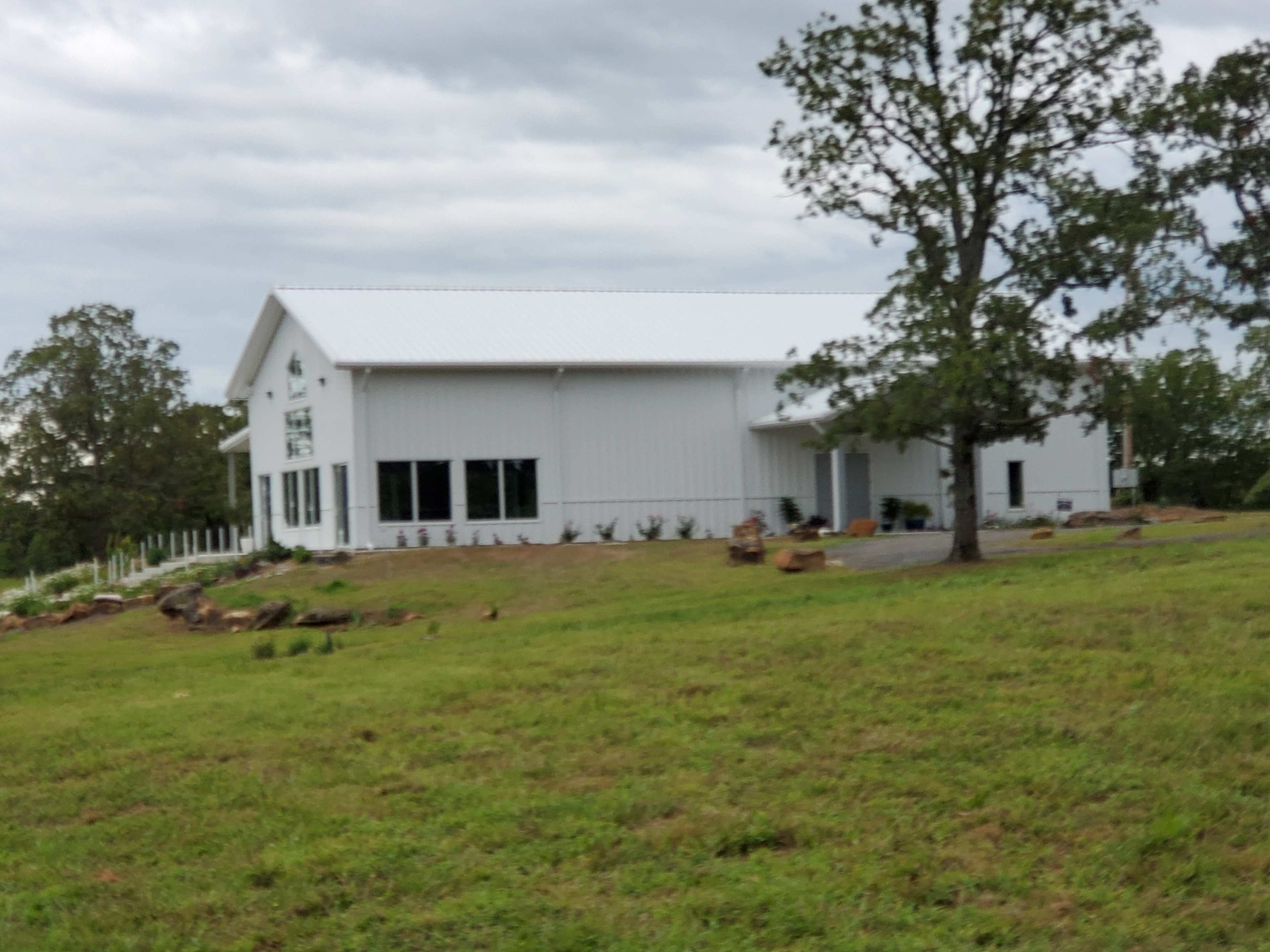 A modern white metal building situated on a grassy field, accompanied by a few trees and landscaping.