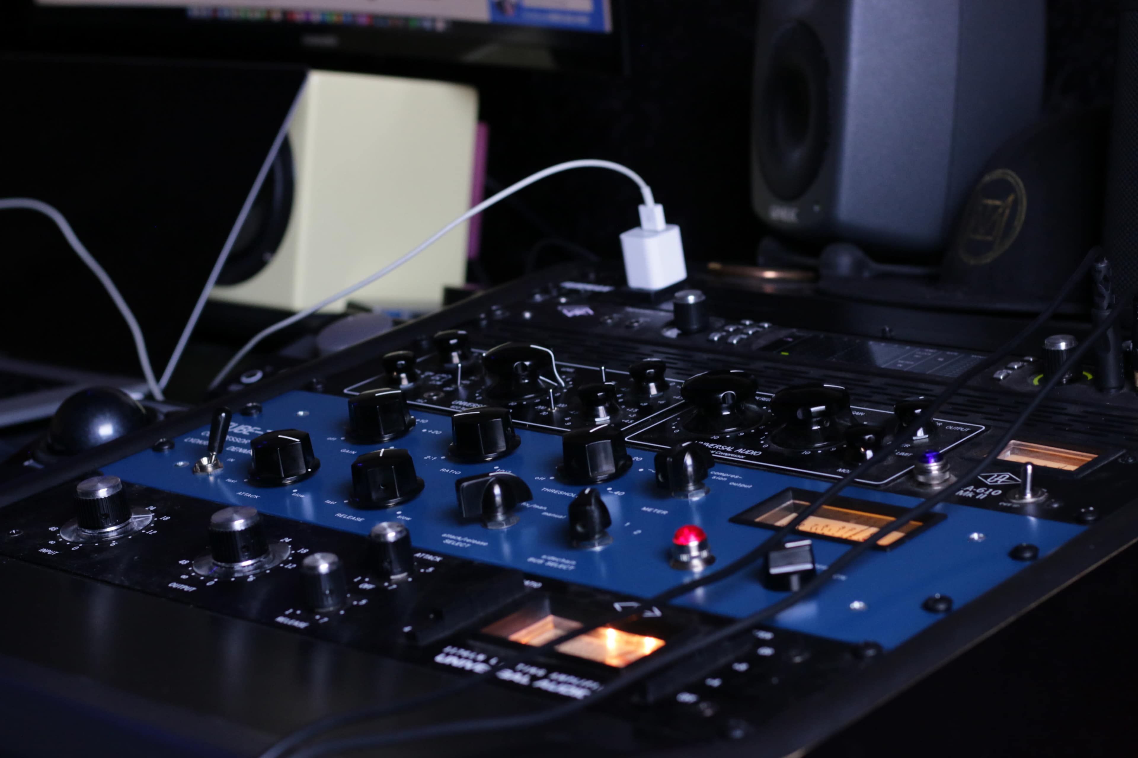 The image shows a close-up of a sound mixing console with various knobs, switches, and a connected charging cable.