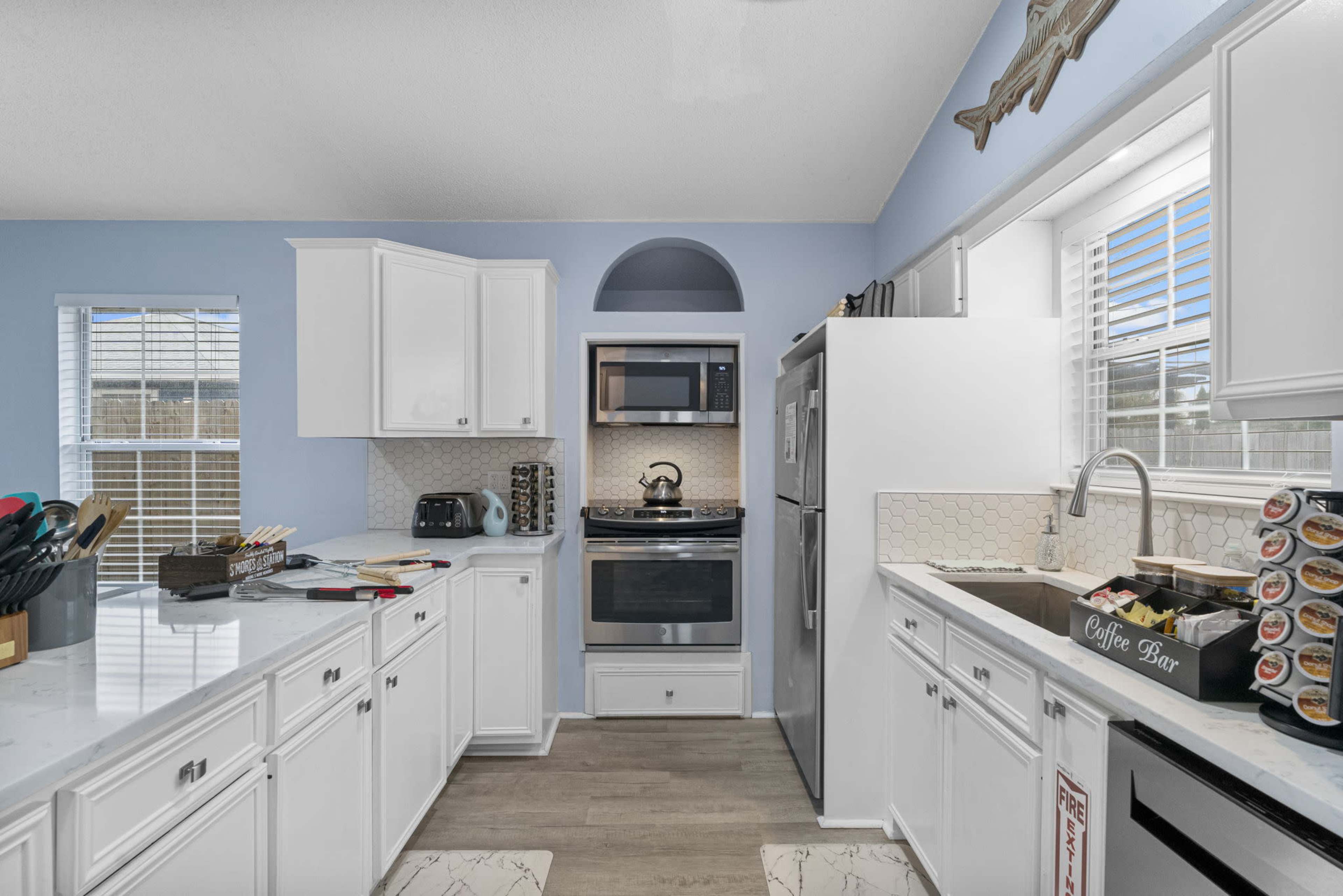 A bright kitchen with white cabinets, a stainless steel microwave and oven, and a sink beneath a window.