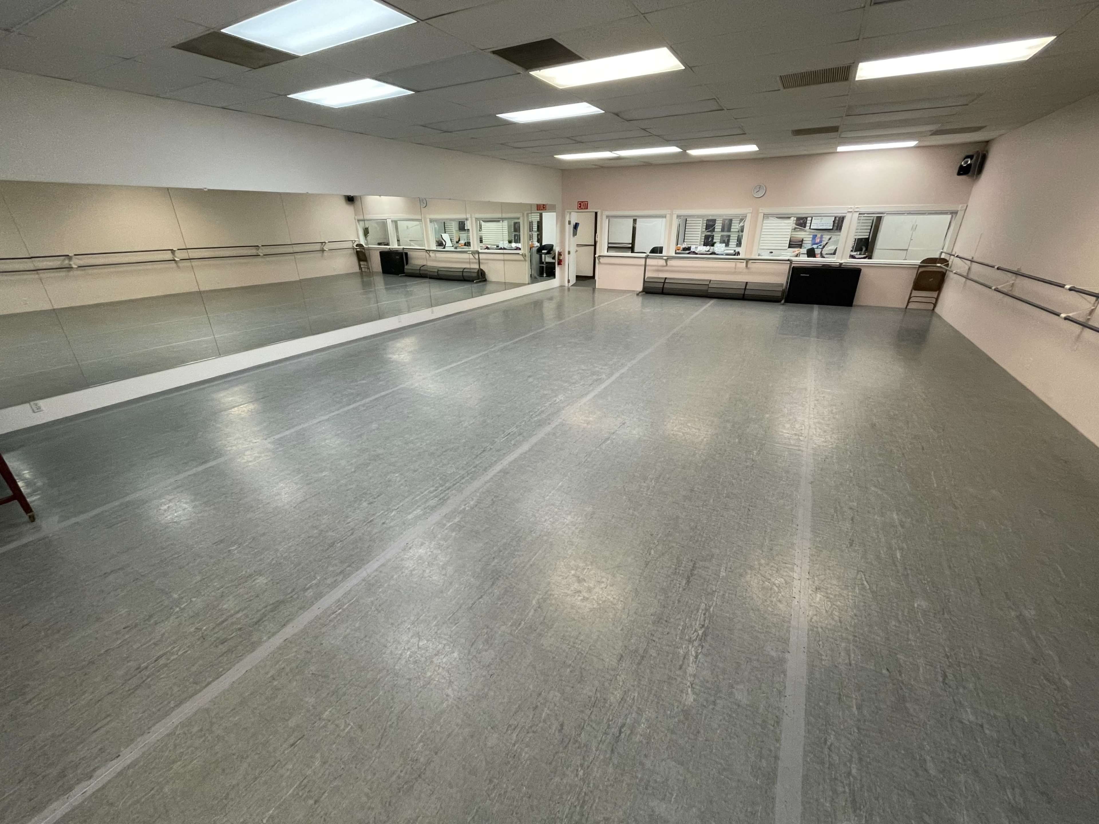A spacious dance studio with mirrored walls, wooden ballet bars, and a polished gray floor.