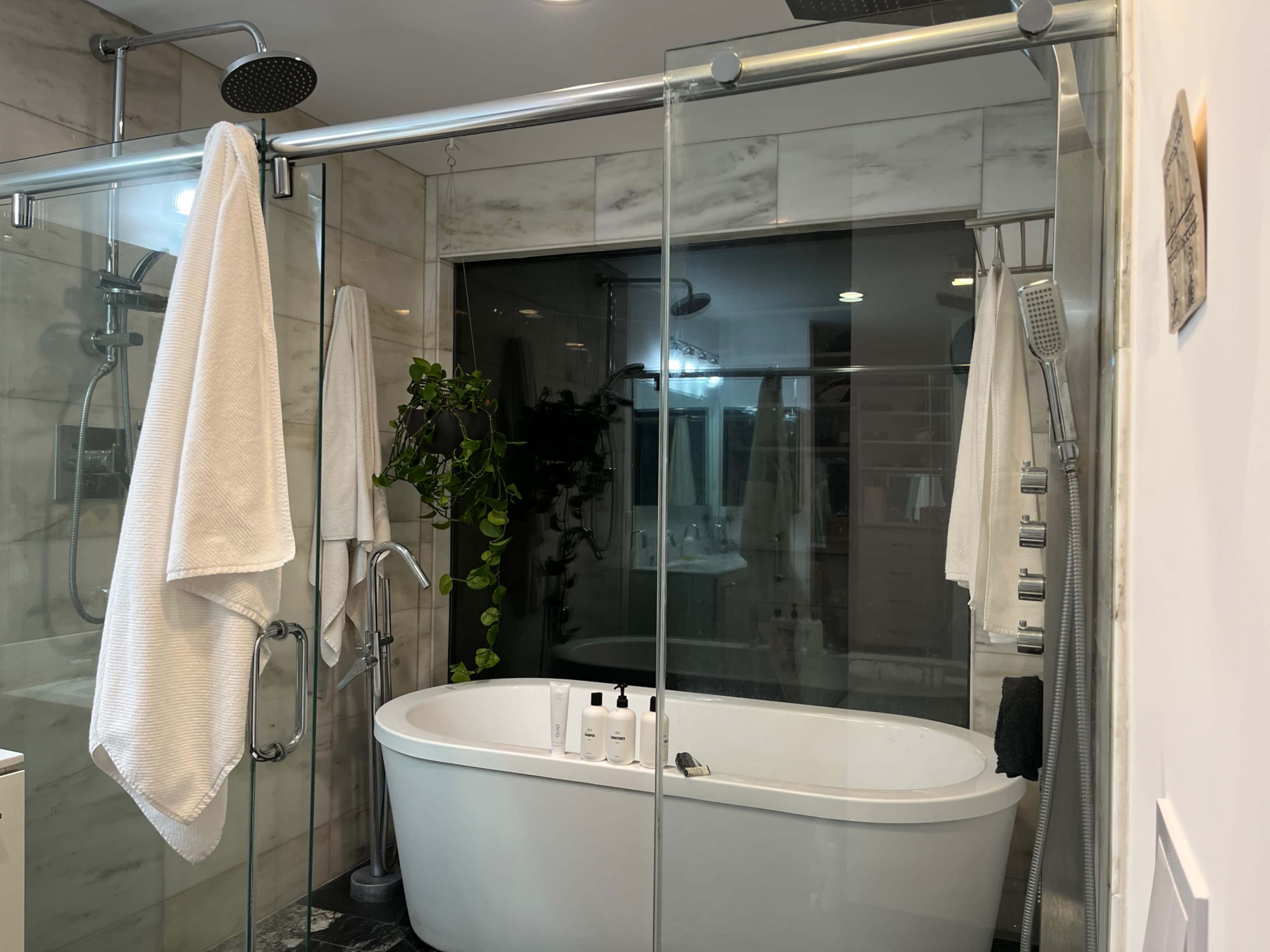 The image shows a modern bathroom featuring a freestanding bathtub, a glass-enclosed shower area, and white towels hanging on glass panels.