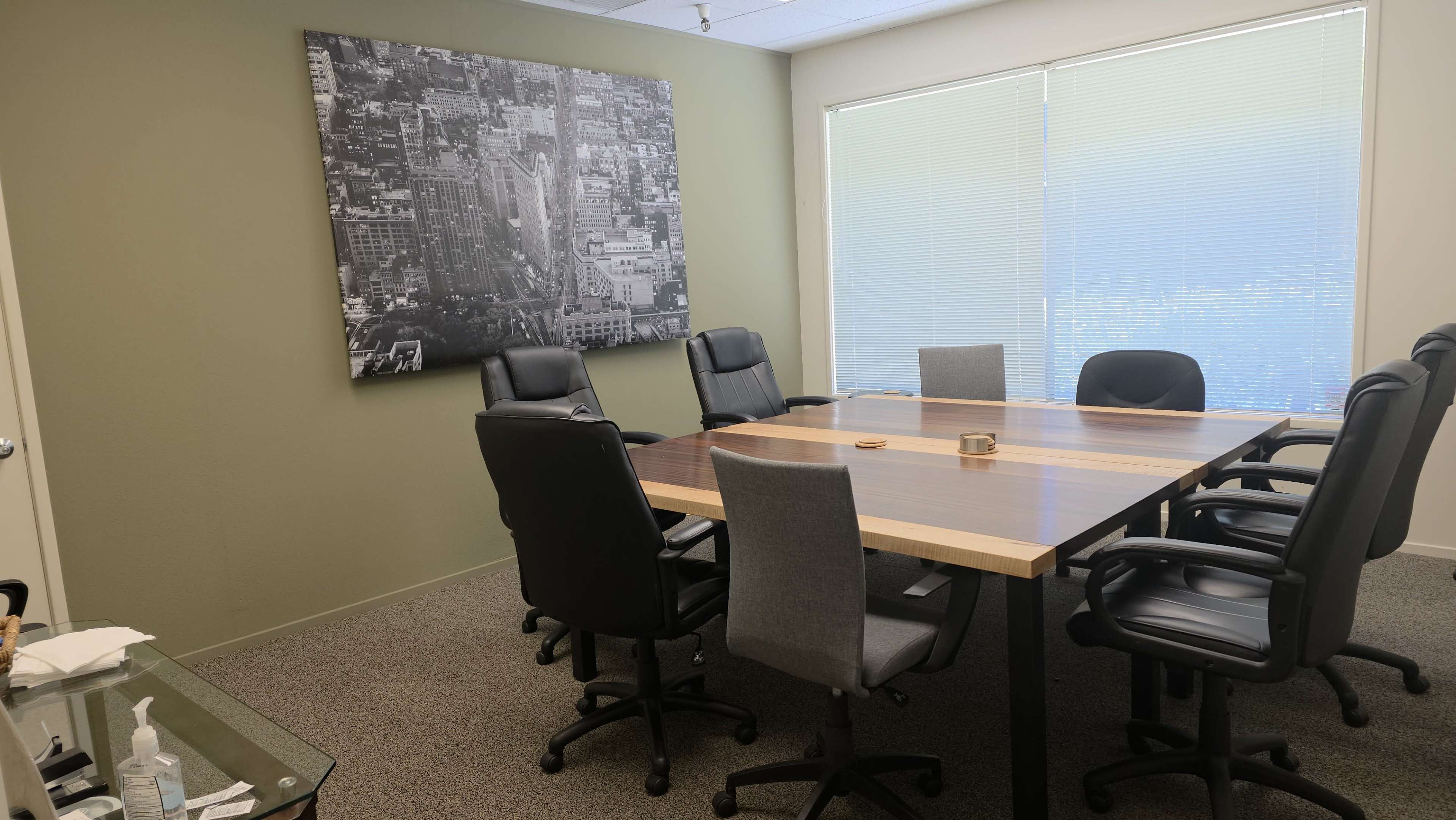 The image shows a conference room with a large wooden table surrounded by chairs and a black-and-white photograph on the wall.