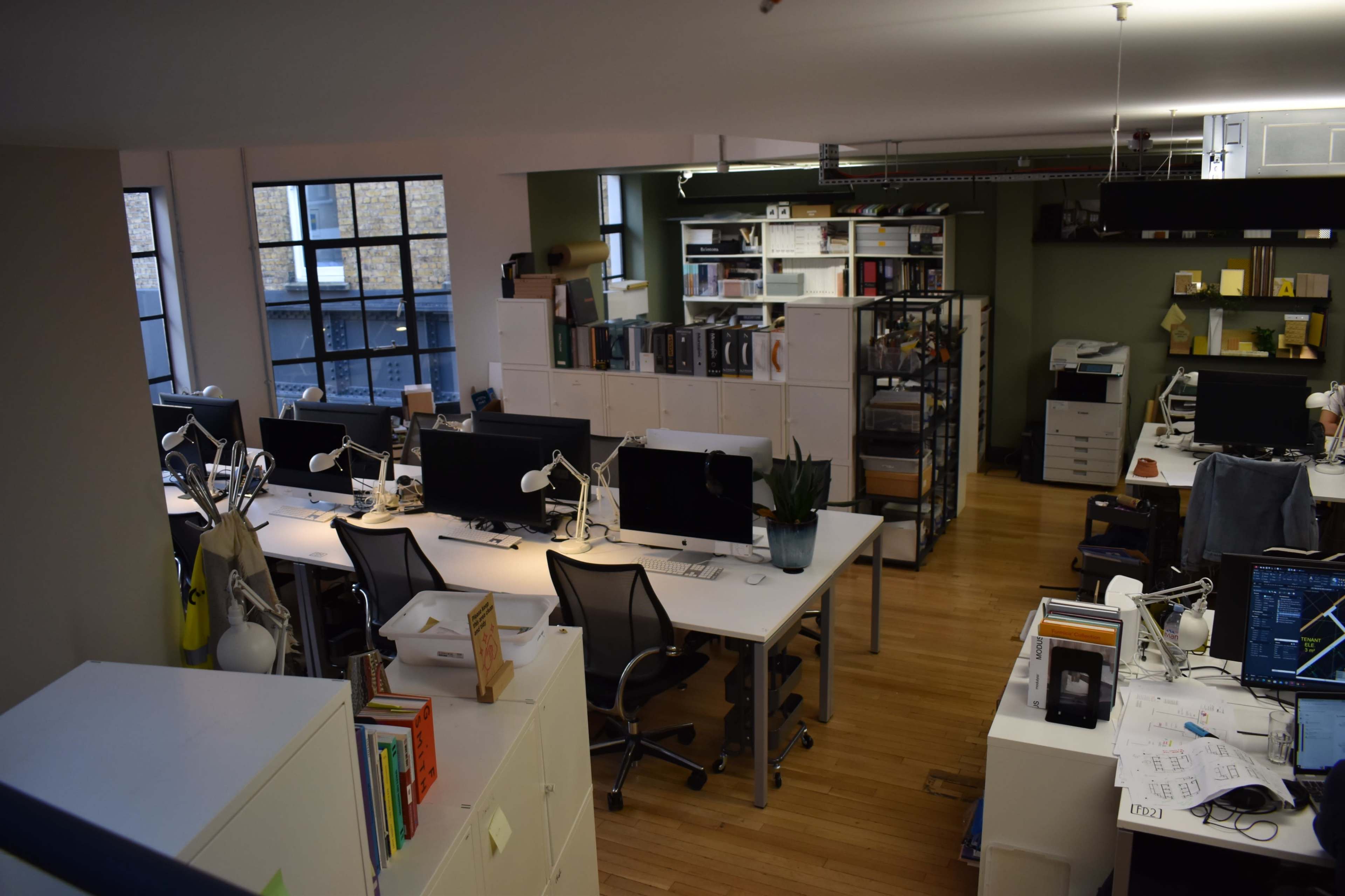 The image shows a modern office space with multiple workstations, computer desks, and organized shelving units.