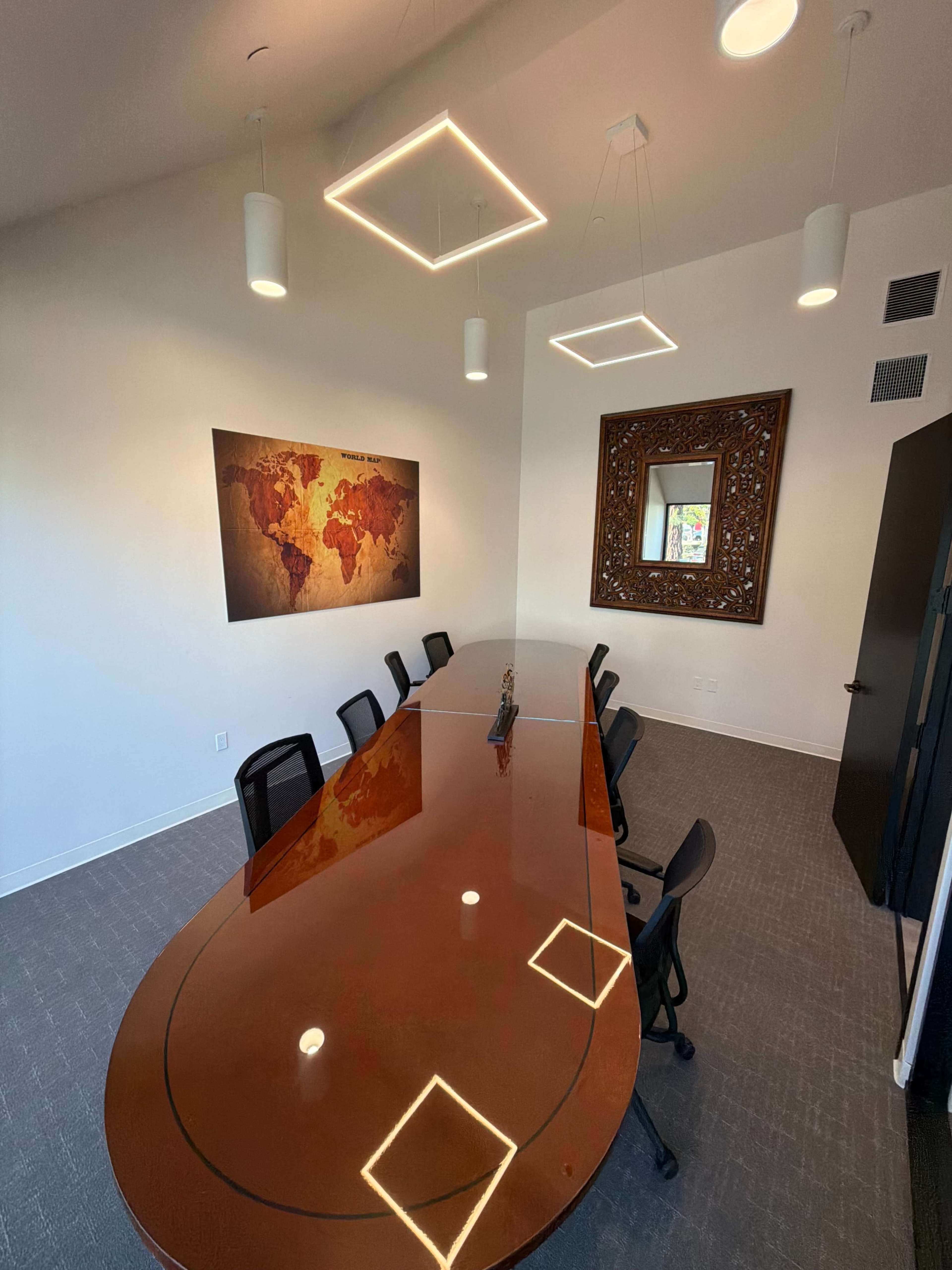 The image shows a modern conference room with a large oval table surrounded by black chairs, featuring a world map on the wall and decorative ceiling lights.