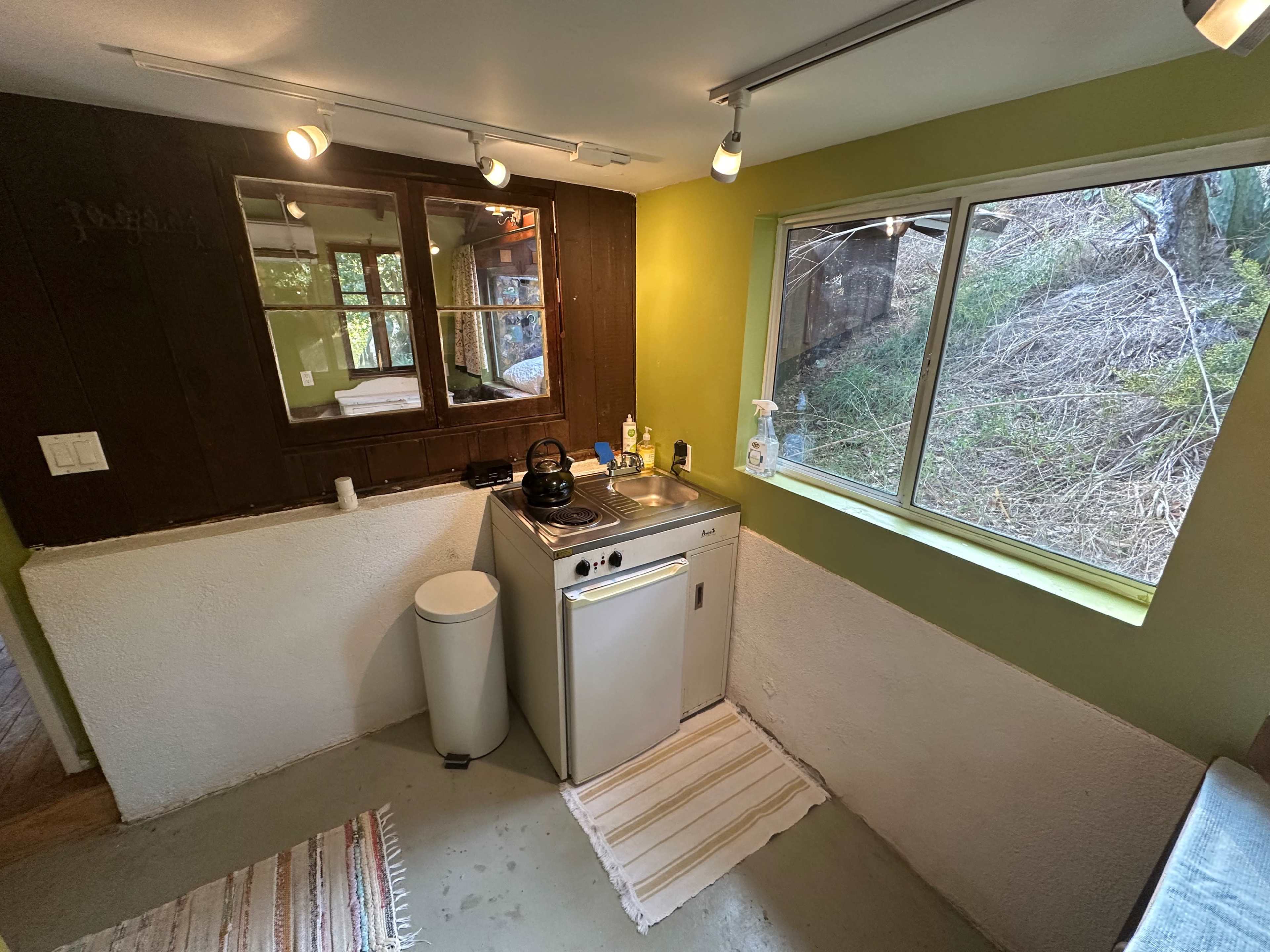 A small kitchen area with a sink, stove, and window overlooking a wooded landscape.
