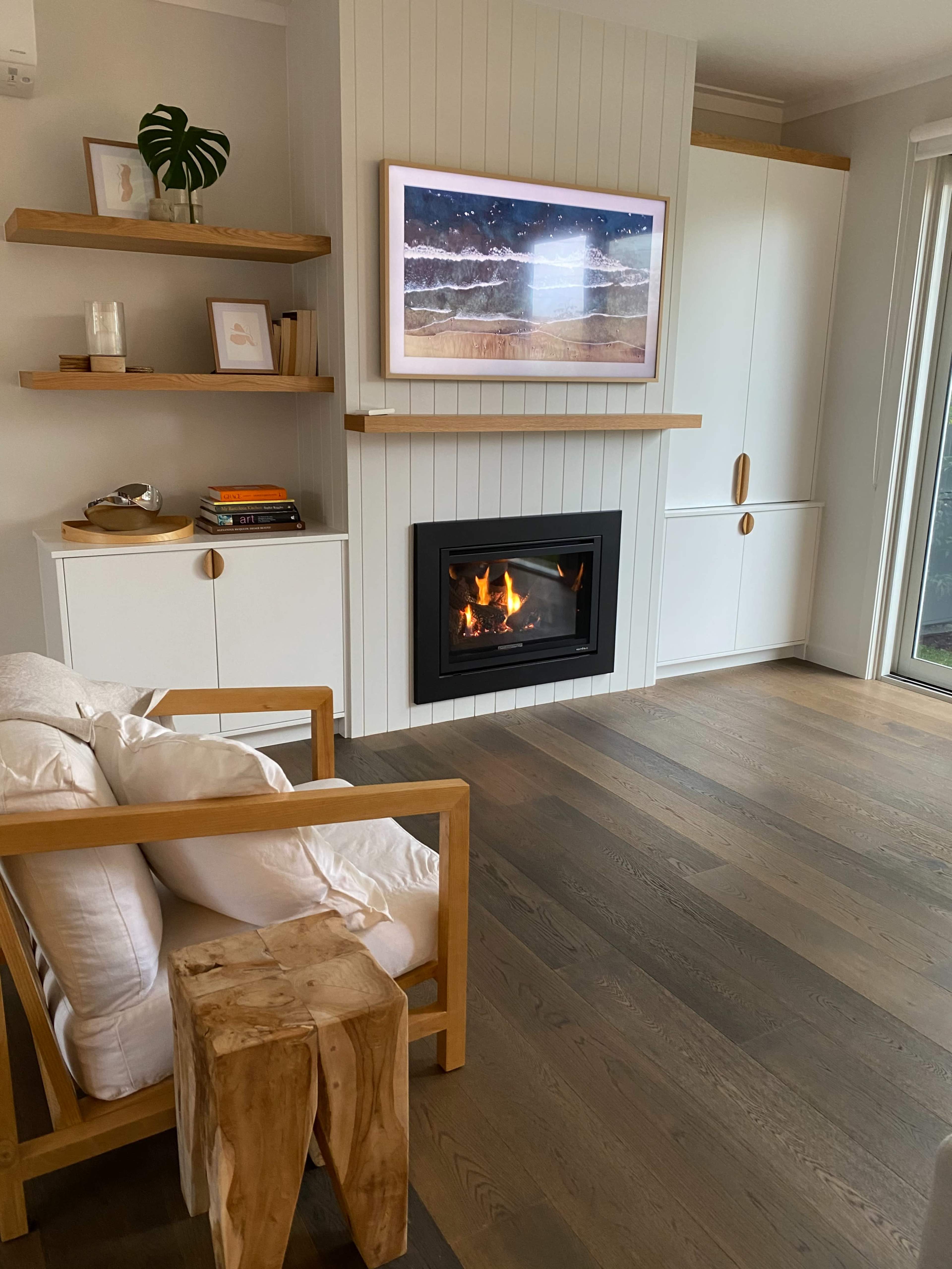 A cozy living room with a modern fireplace, a framed artwork on the wall, wooden furniture, and light hardwood flooring.