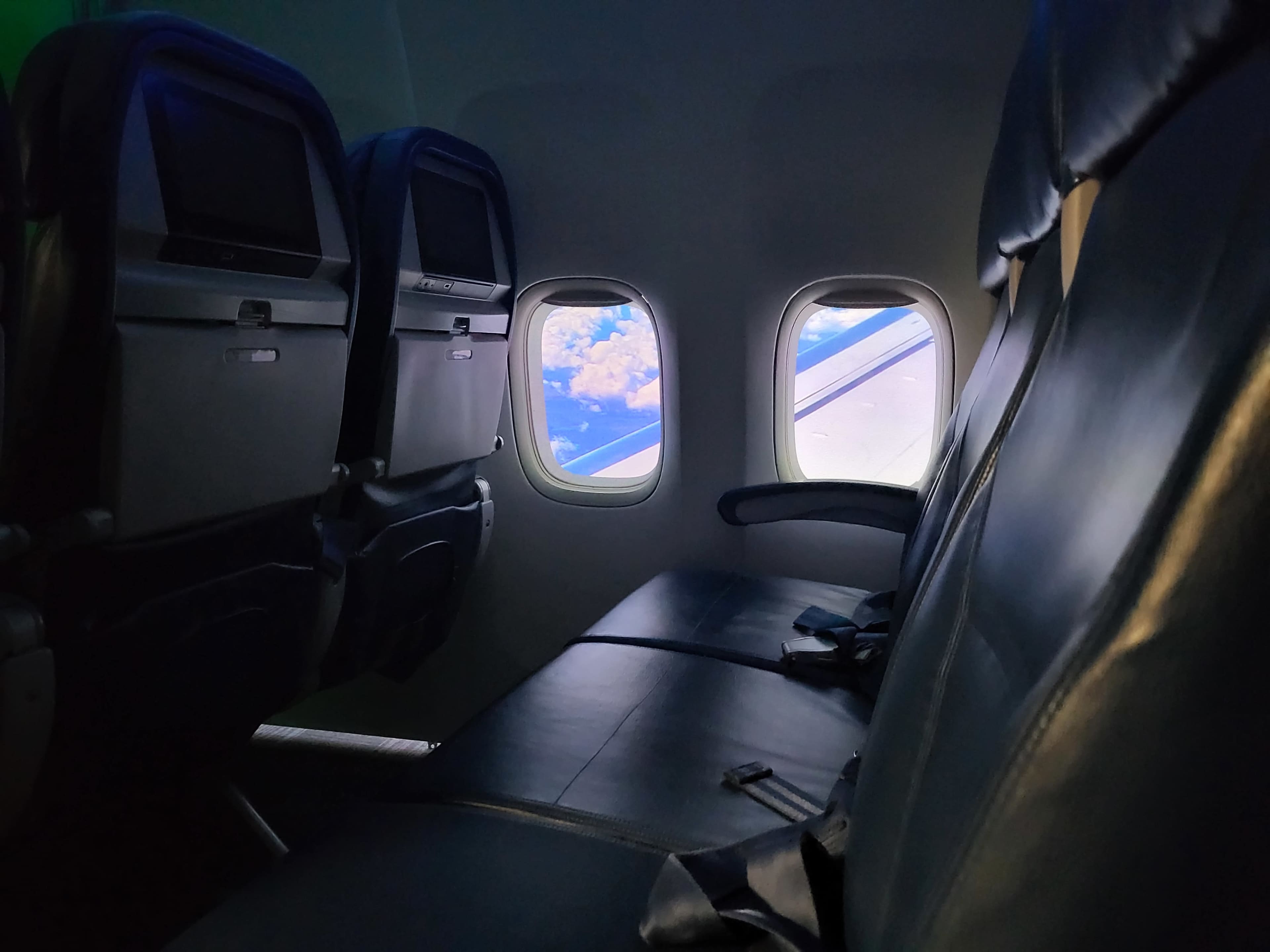 An airplane interior with two empty seats and a view of clouds outside the window.