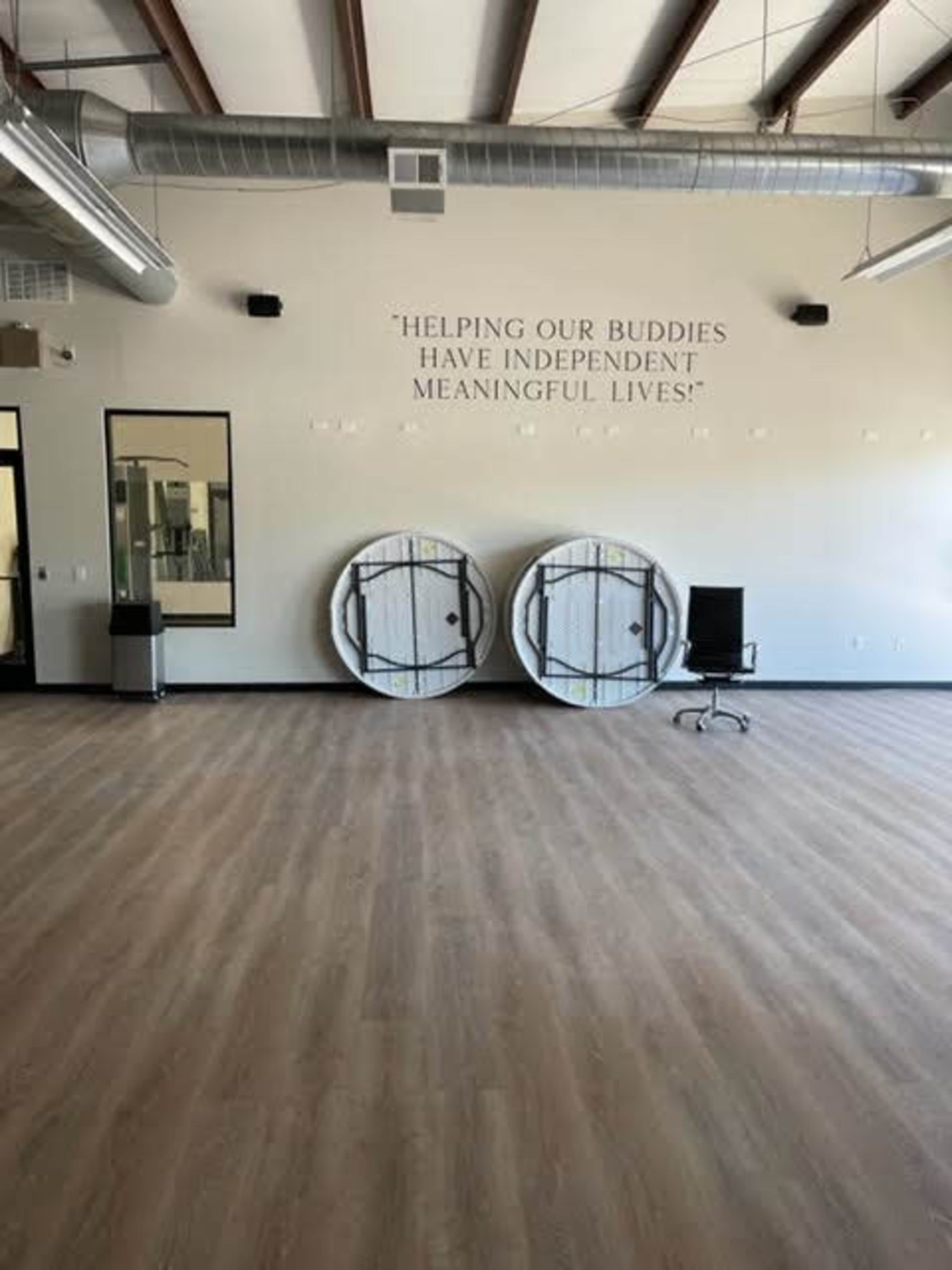 A spacious room with two large round white storage containers against a wall, which features the text "HELPING OUR BUDDIES HAVE INDEPENDENT MEANINGFUL LIVES."