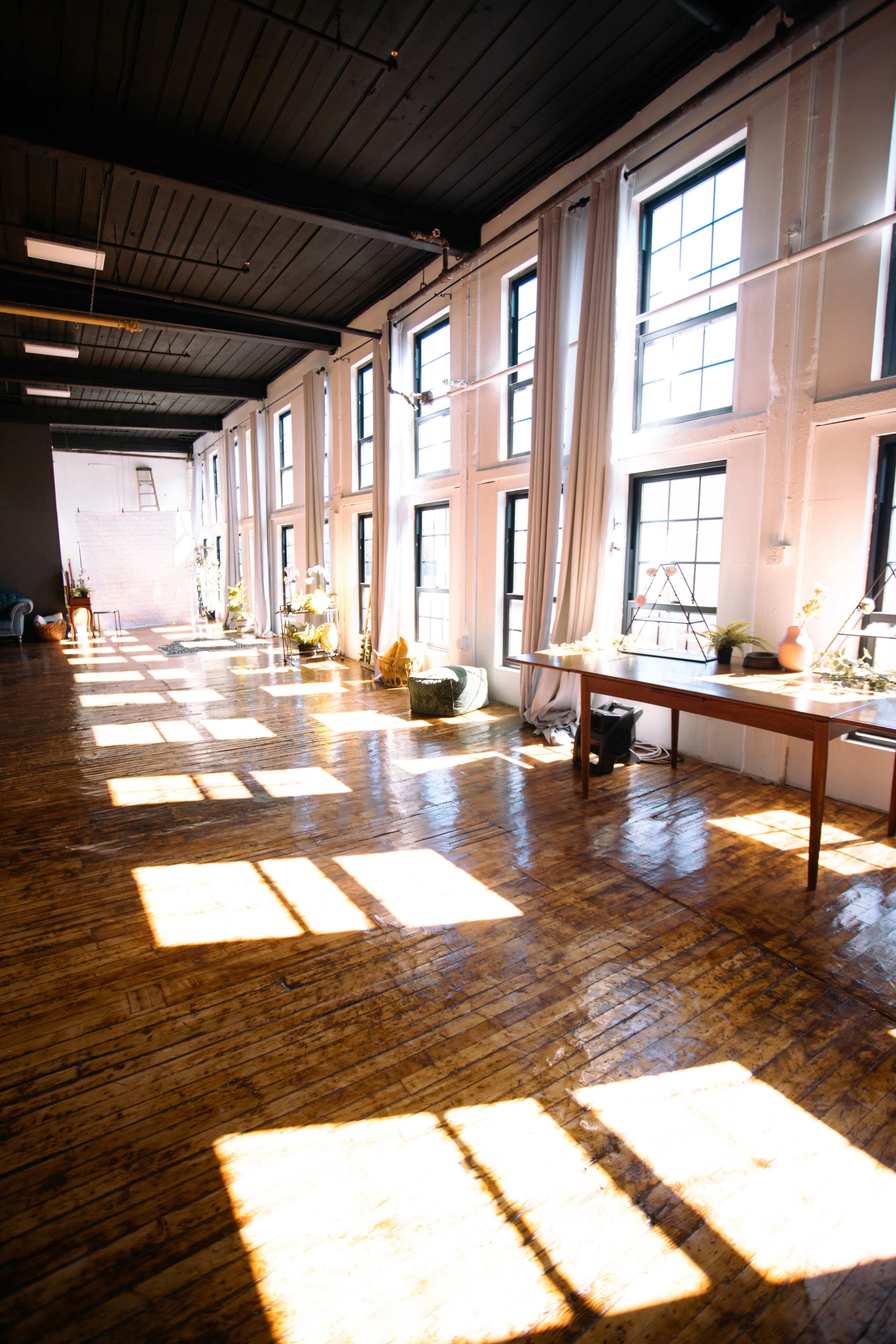 A spacious room with large windows that create a pattern of sunlight on the wooden floor.
