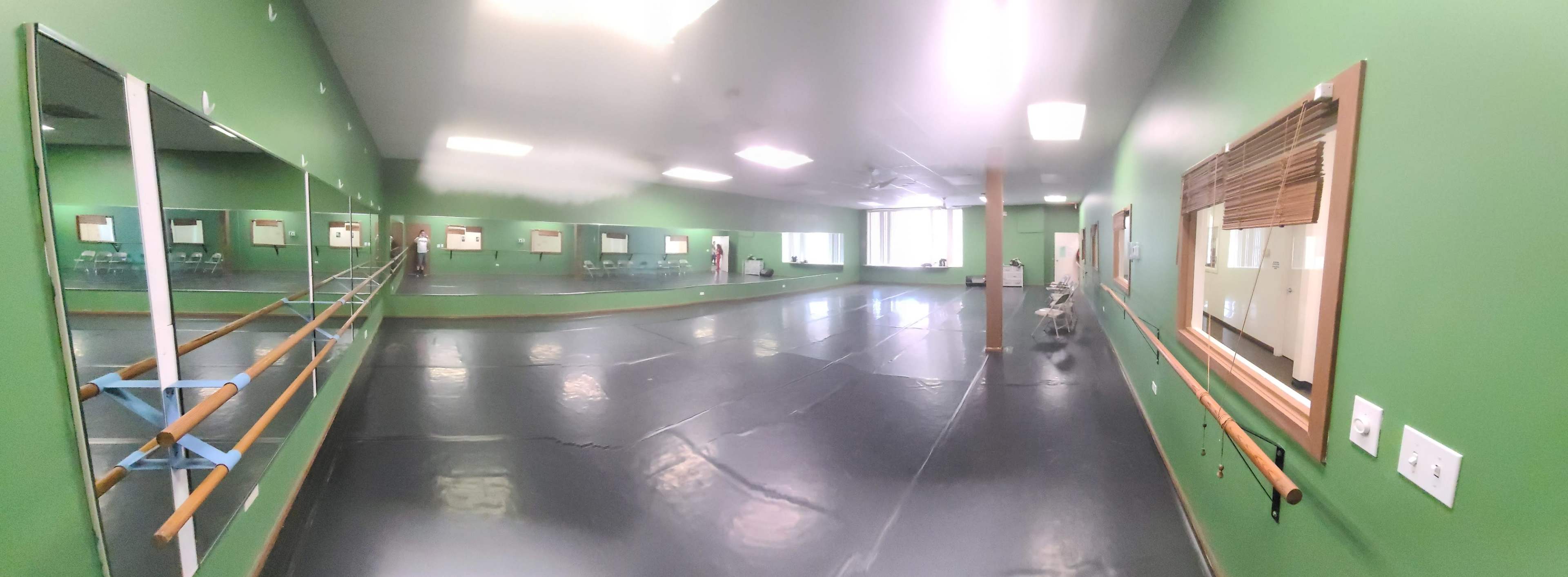 A spacious dance studio with green walls, a mirrored wall, and ballet barres lining the sides.