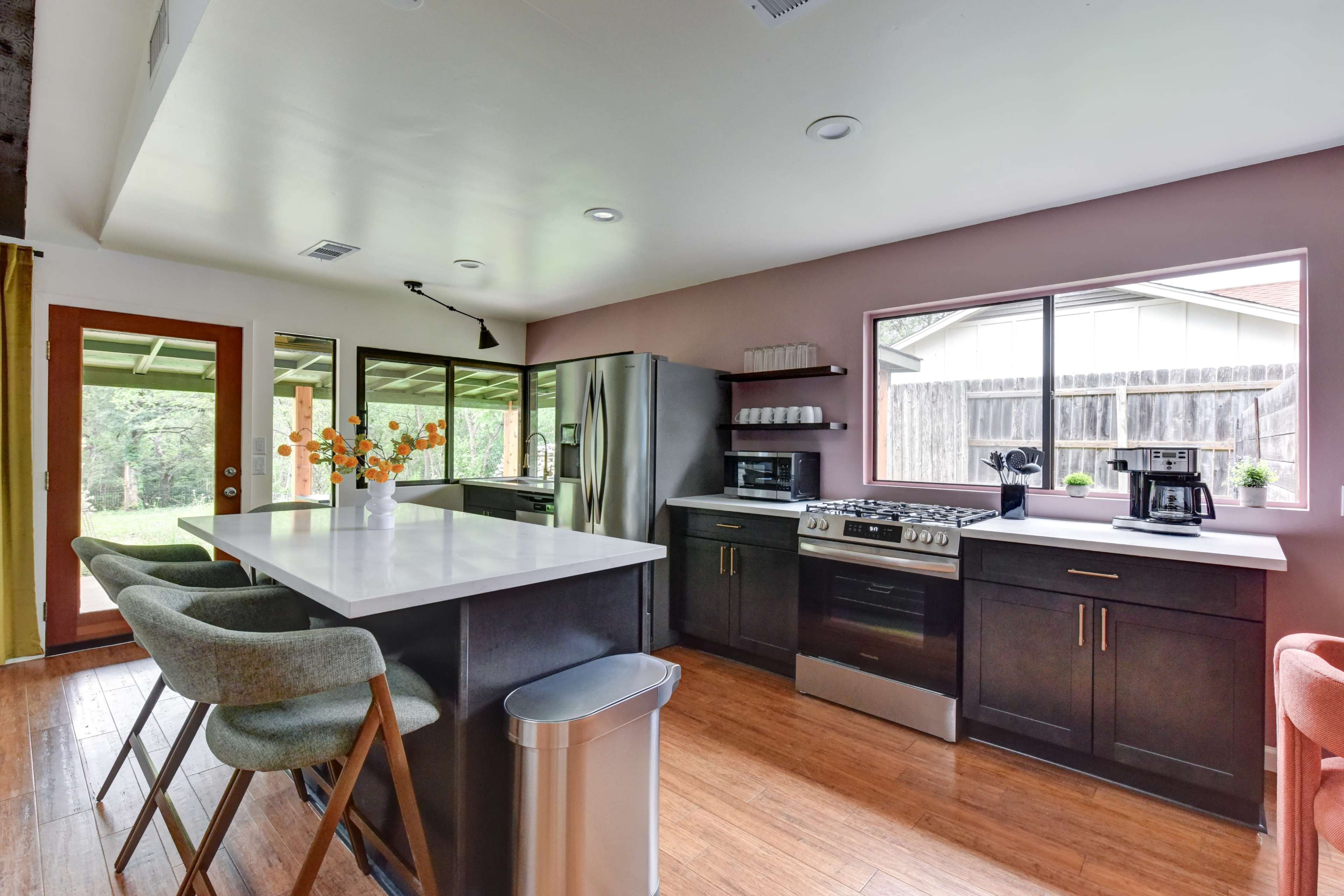 The image shows a modern kitchen with dark cabinetry, stainless steel appliances, and a central island with bar seating.