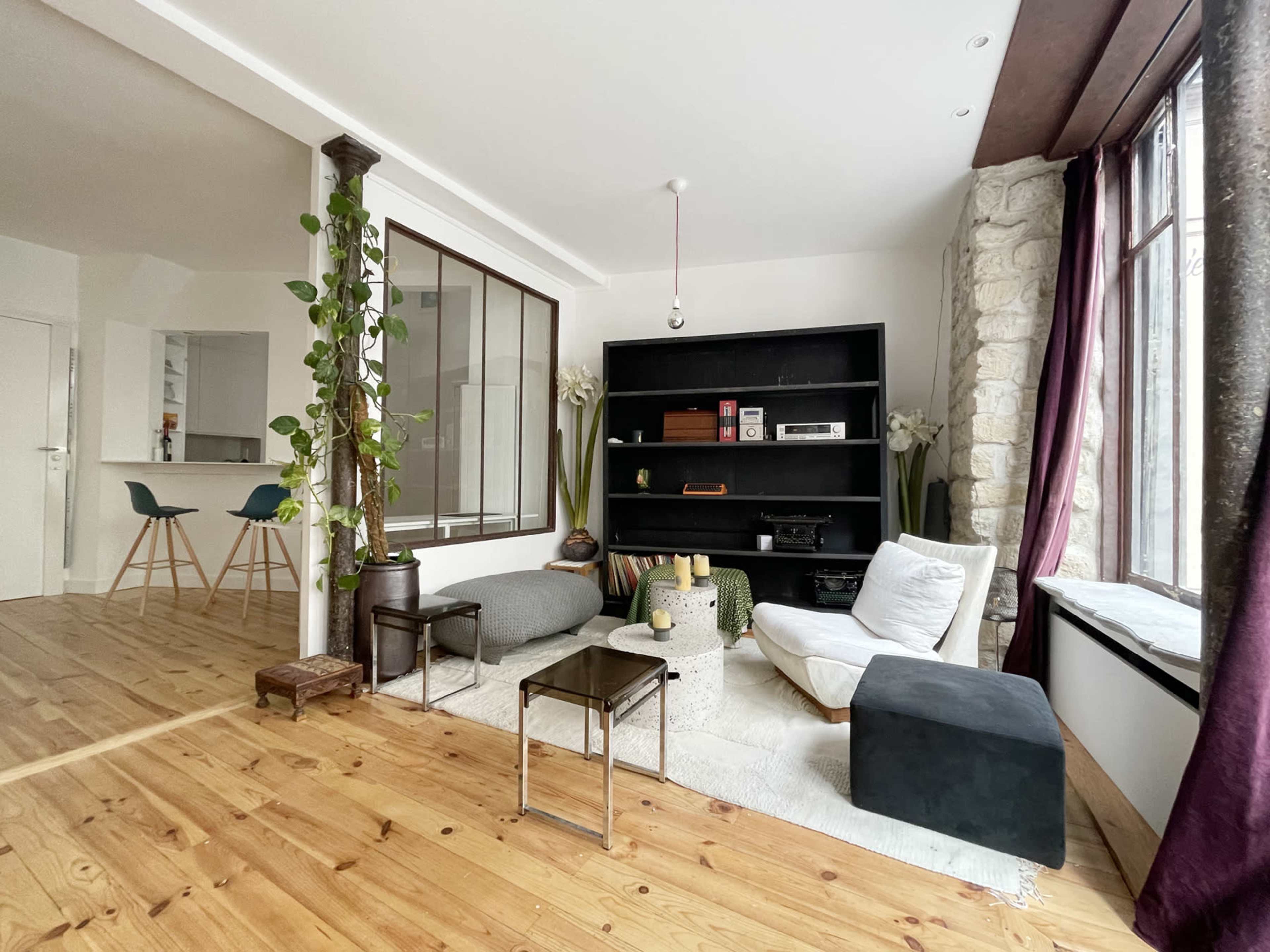 A modern living room featuring a black bookshelf, various seating options, and large windows with natural light.