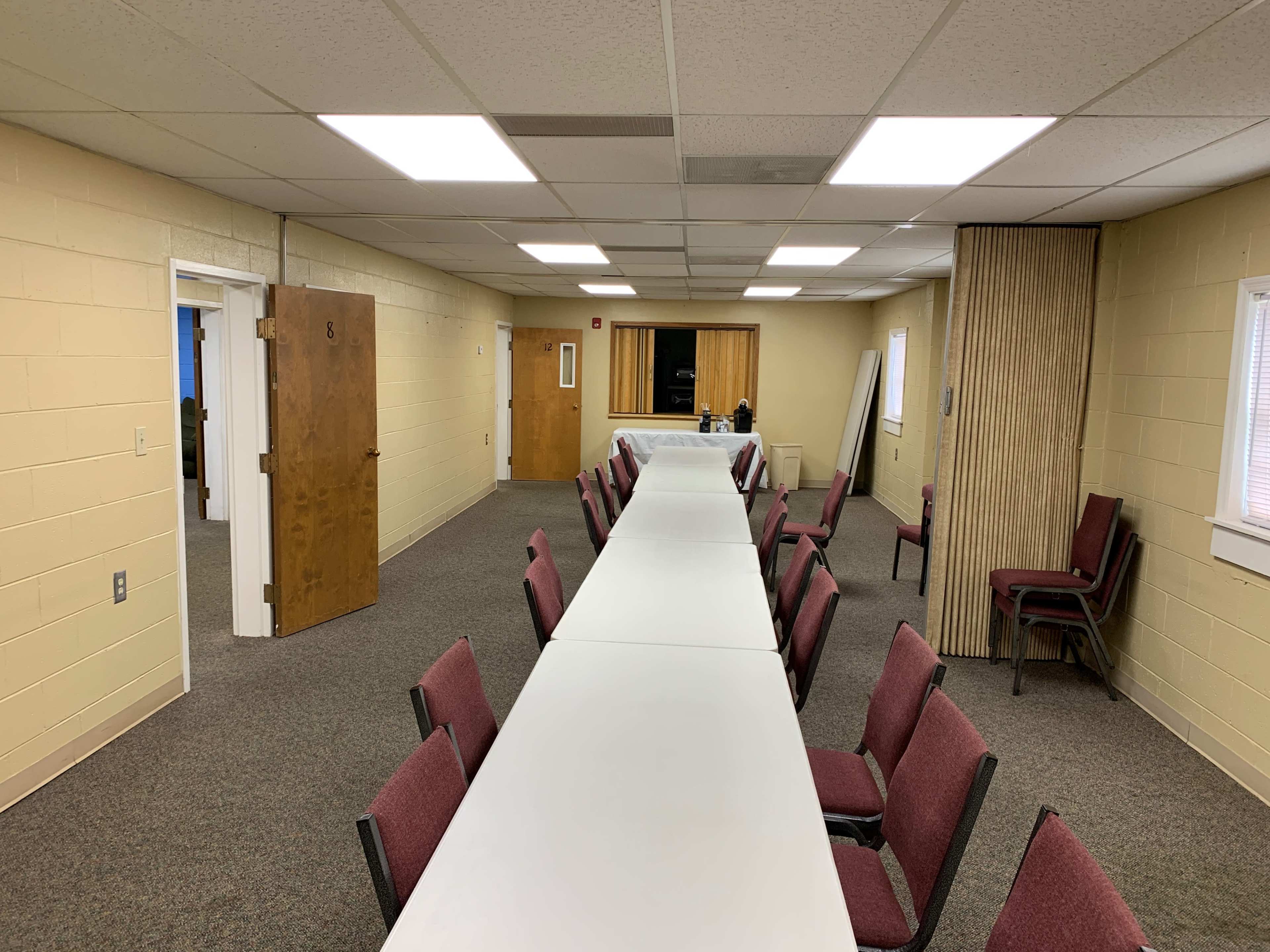 A long table is set up in a spacious meeting room with several chairs arranged around it, and doors leading to adjacent rooms are visible.