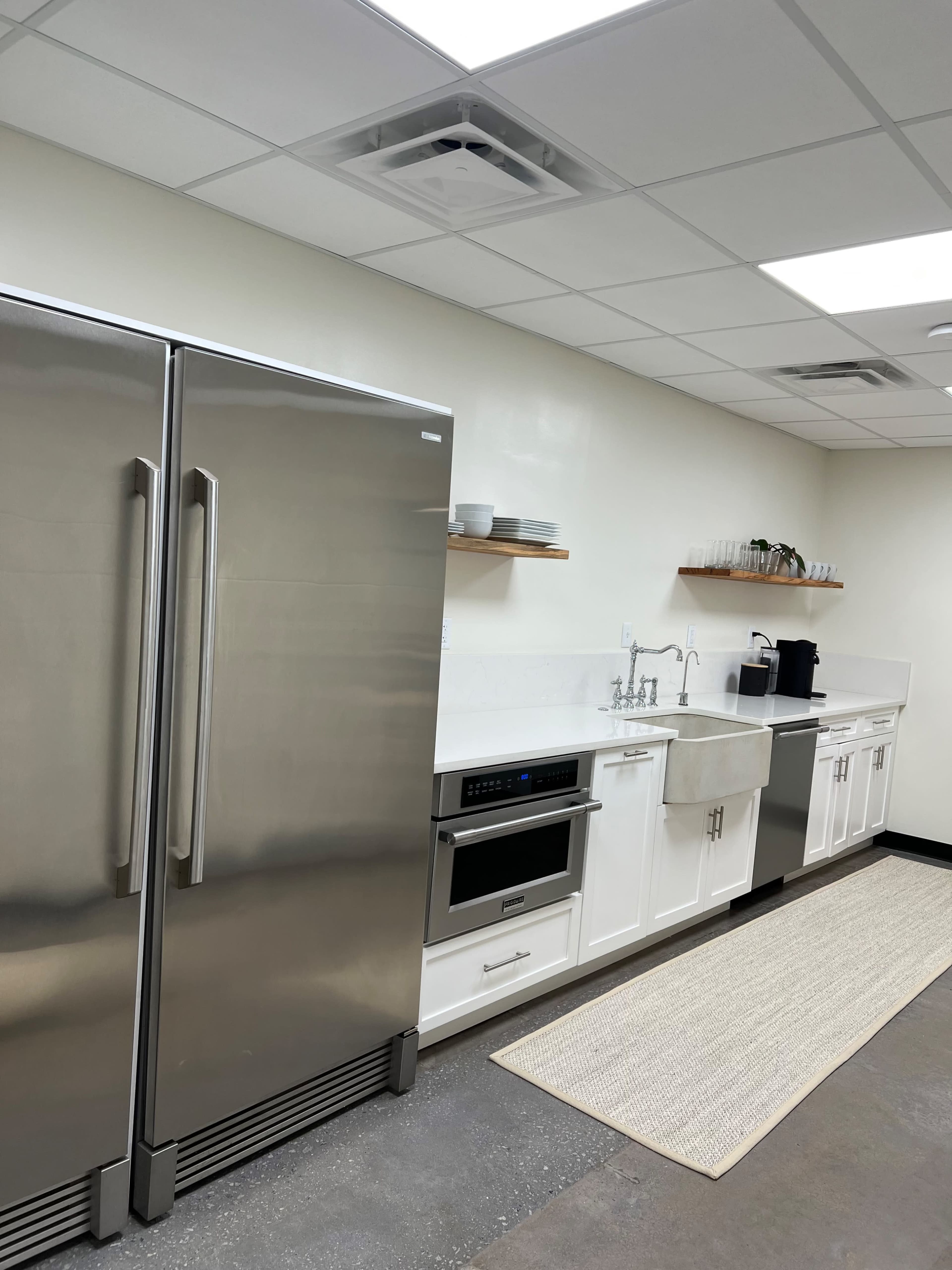 A modern kitchen features stainless steel appliances, white cabinetry, and a sink, with a rug on the floor and shelves holding dishes above.