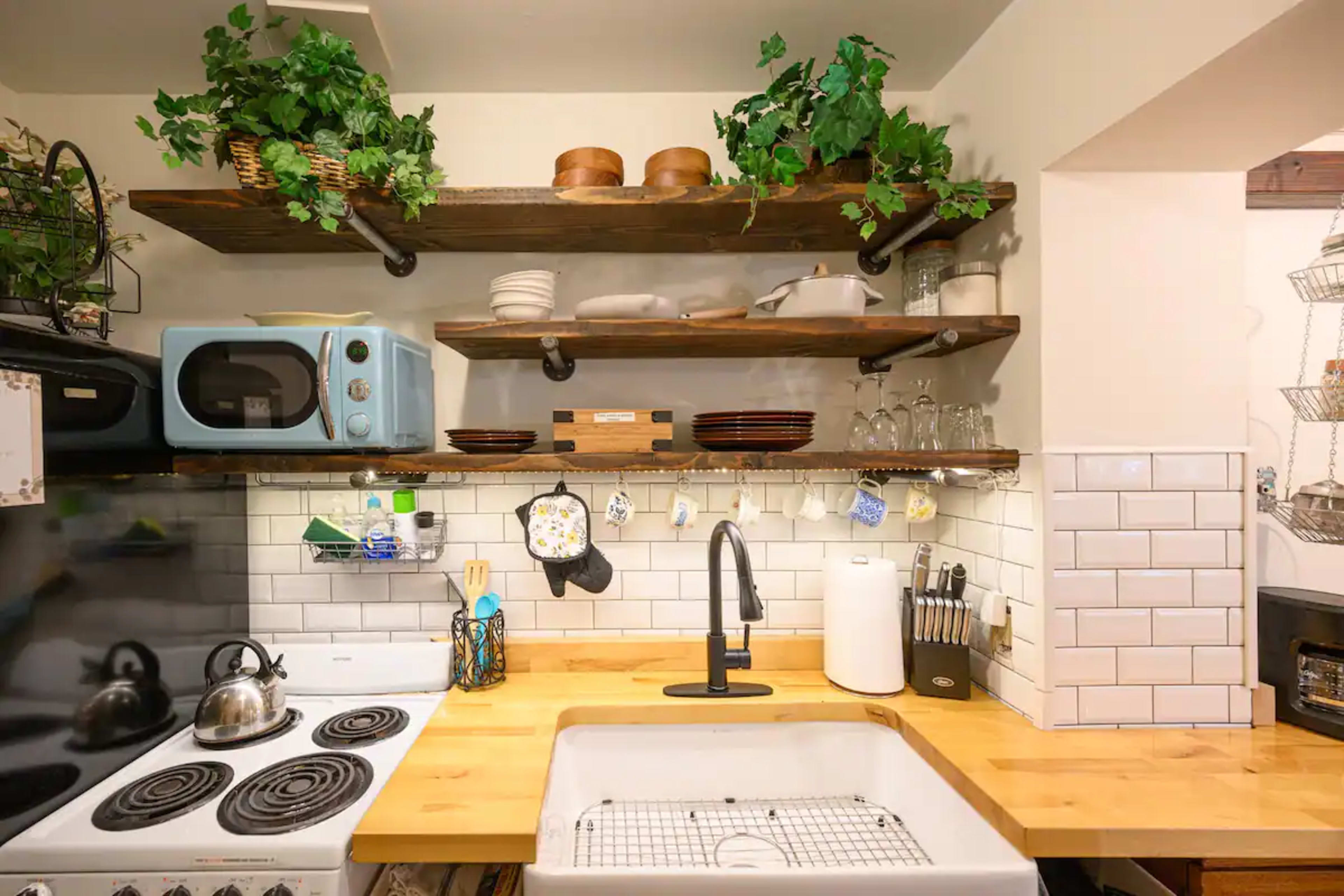 A rustic kitchen with open wooden shelves displaying kitchenware above a farmhouse sink and a stove.