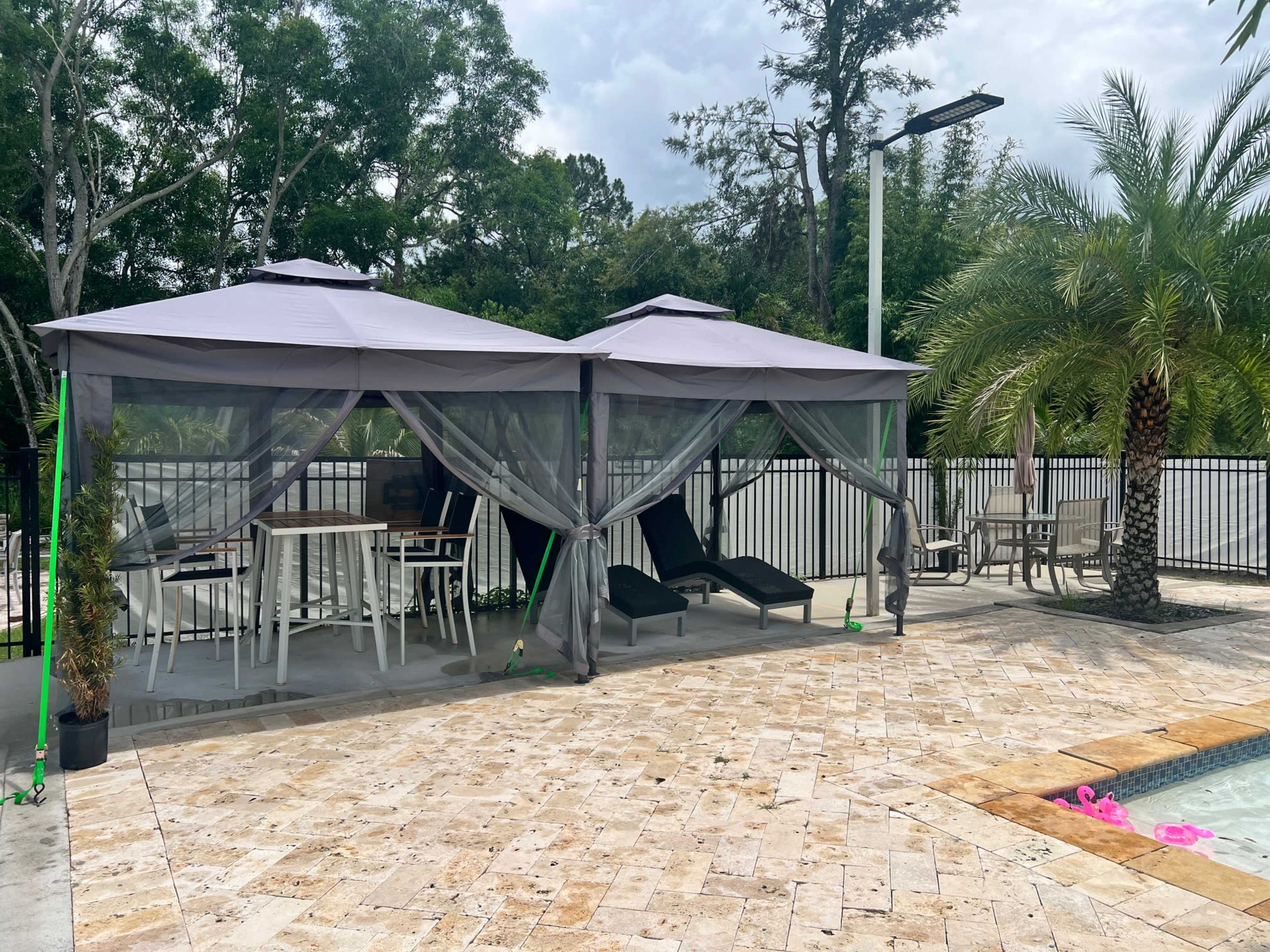 The image shows two gazebo structures with canopy shades adjacent to a pool area, surrounded by tropical plants and lounge chairs.