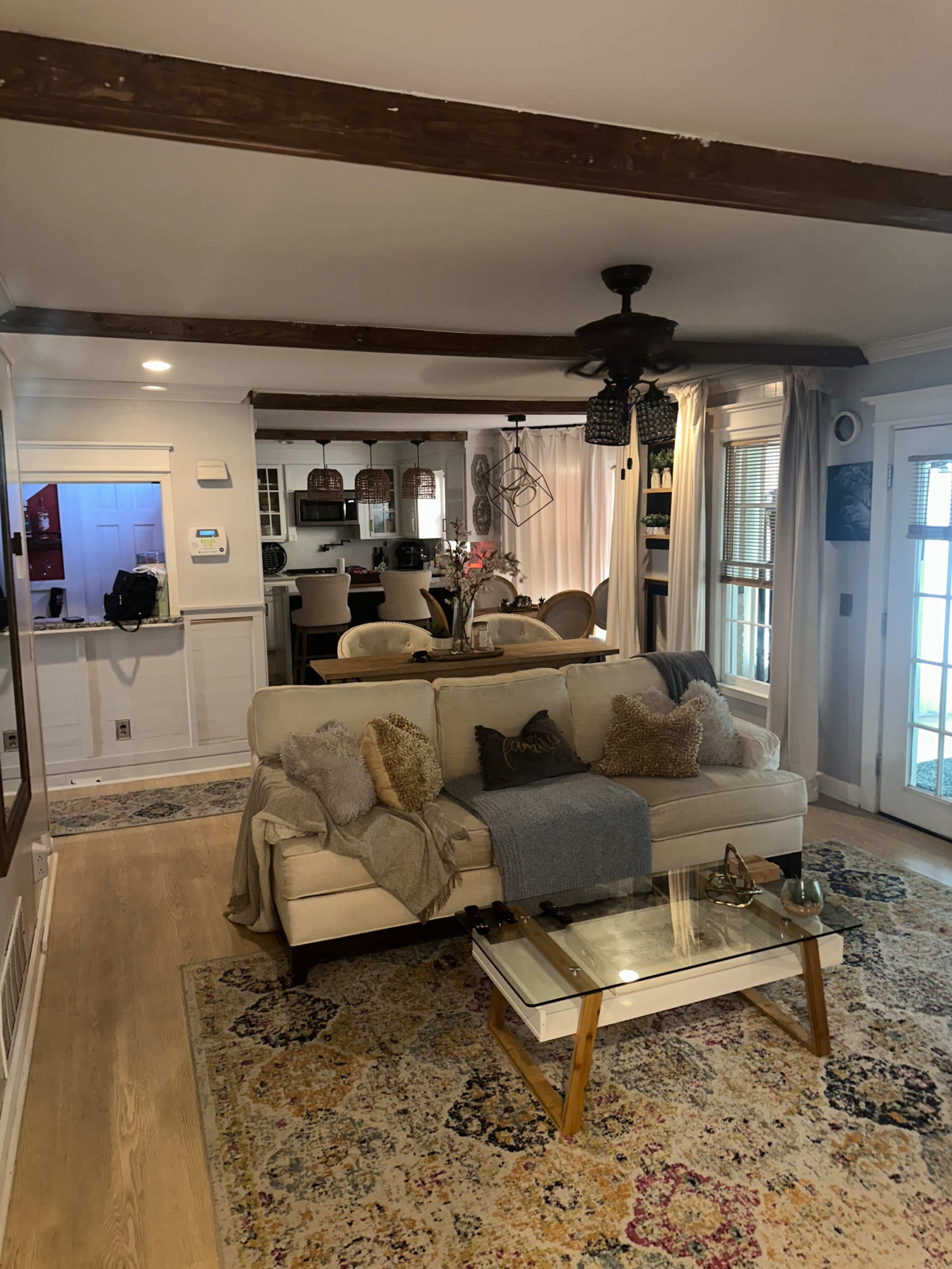 A living room featuring a sofa with decorative pillows, a coffee table, and a dining area visible in the background.