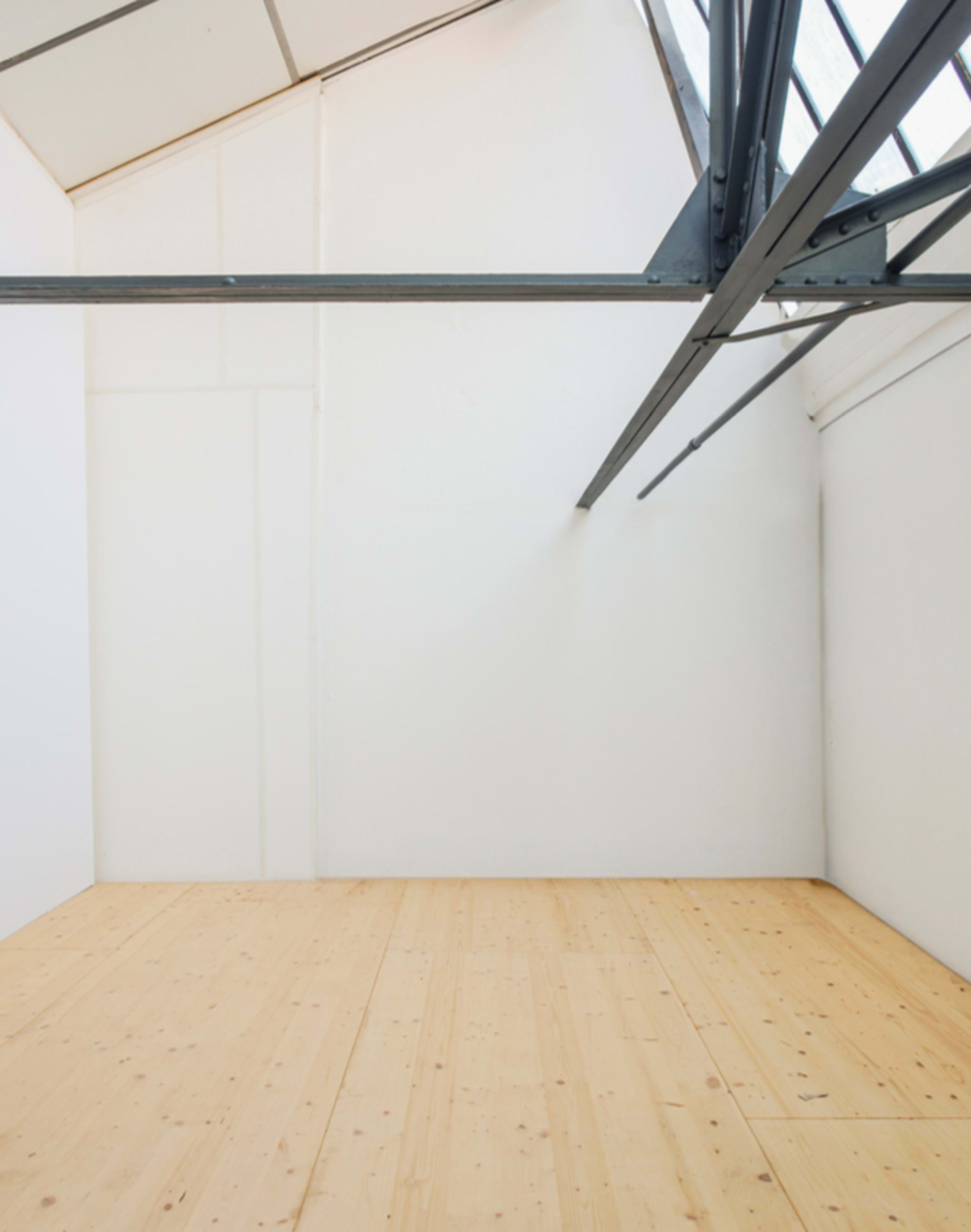 The image shows a minimalistic interior of an empty room with white walls and wooden flooring, featuring exposed metal beams.