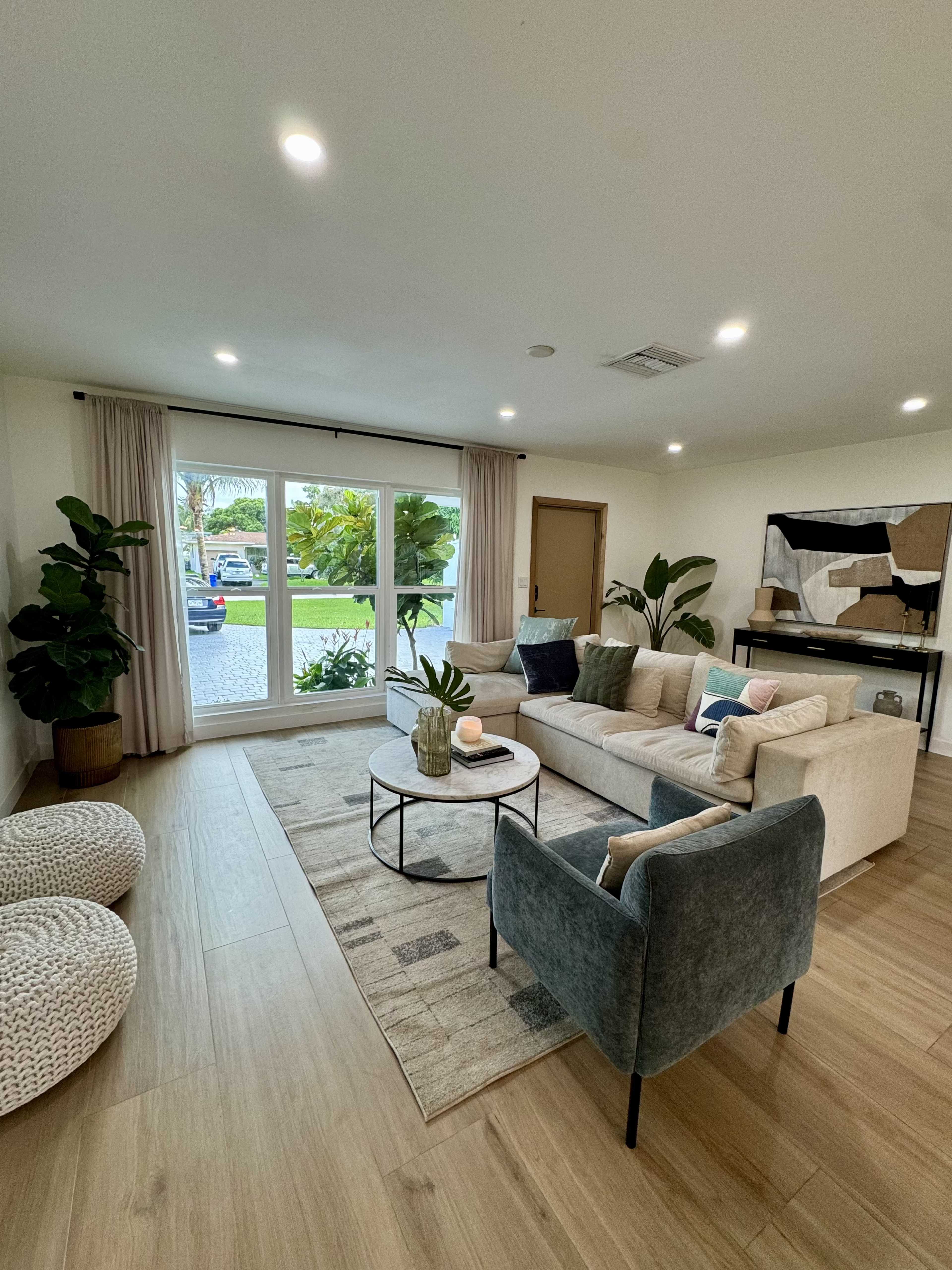 A modern living room features a beige sofa, a circular coffee table, and a large window overlooking a garden area.