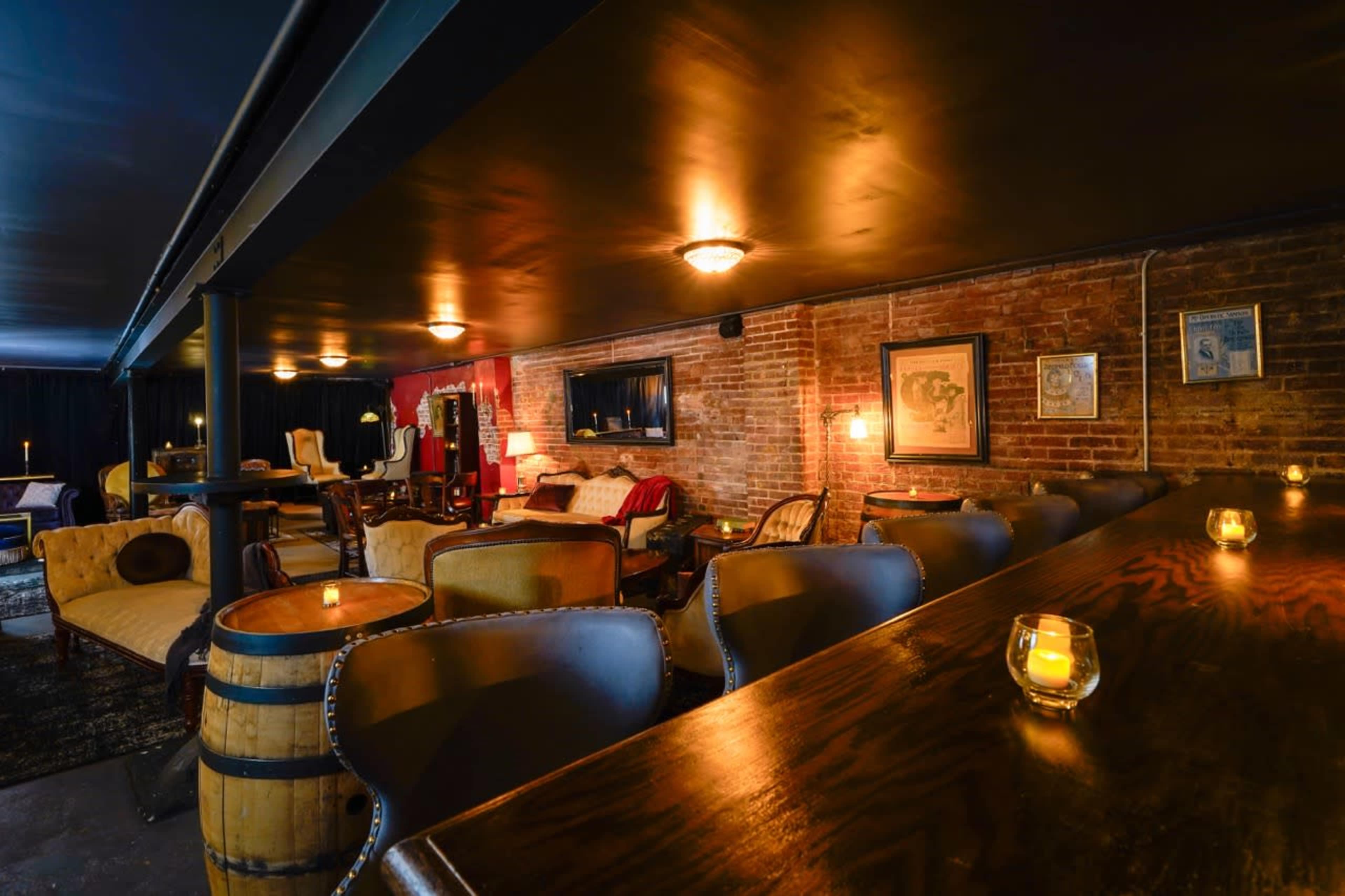 A dimly lit lounge area with brick walls, comfortable seating, and candles on a wooden bar.