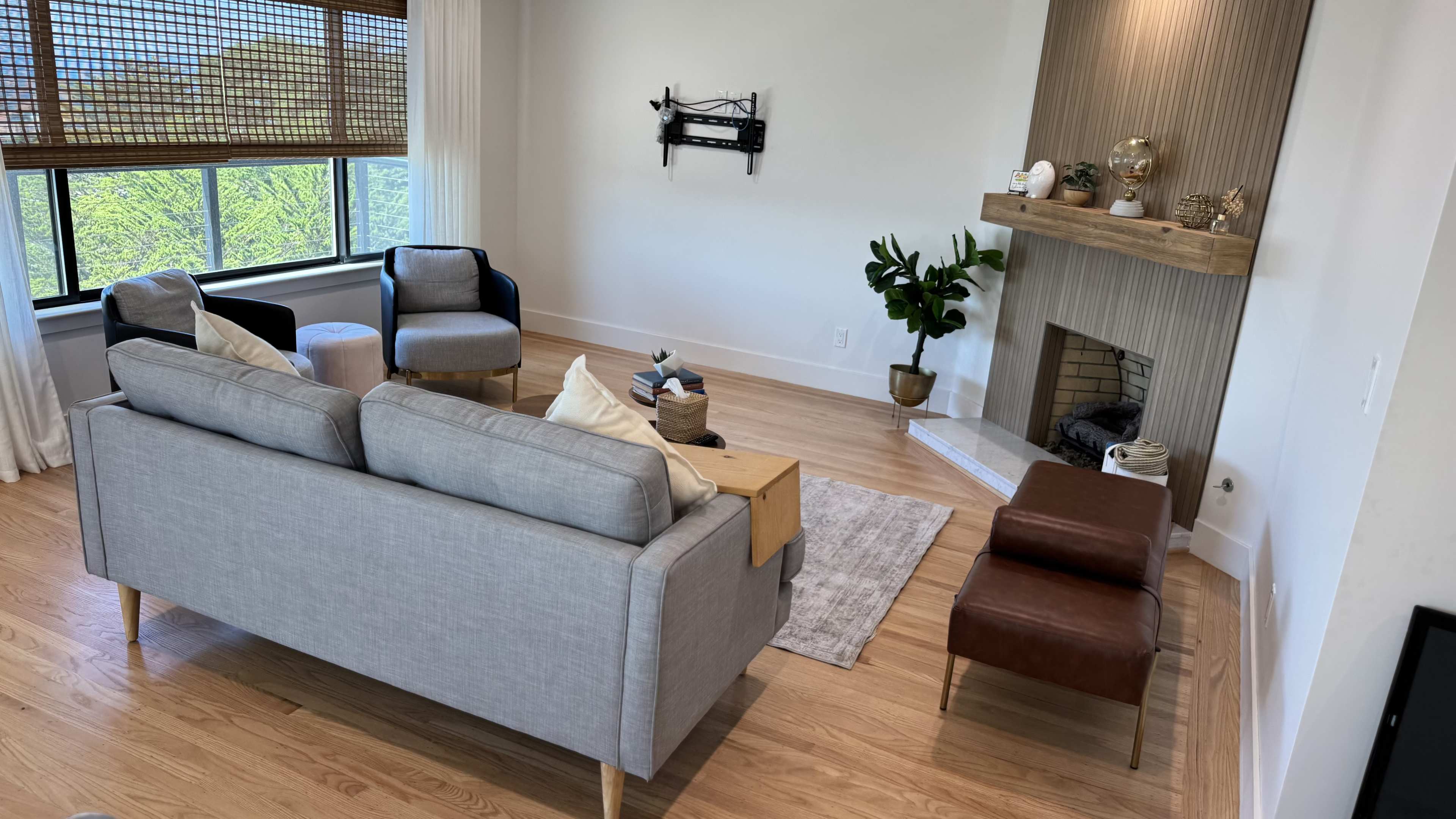 The image shows a modern living room featuring a gray sofa, two armchairs, a wooden coffee table, and a fireplace with decorative items.